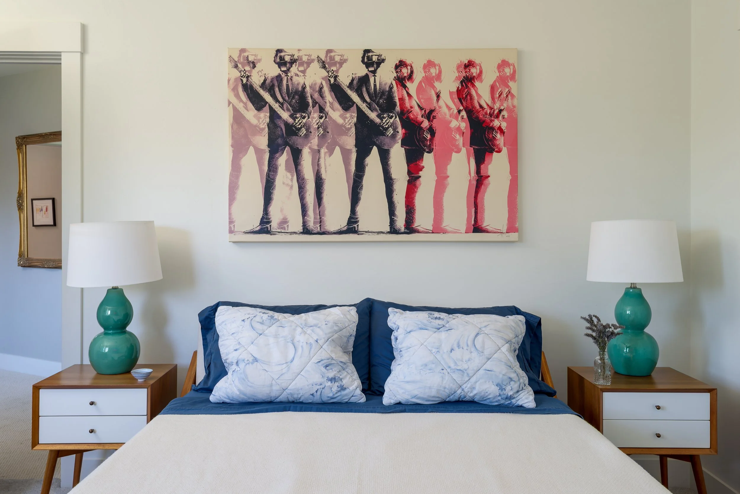A guest bedroom is funky and modern with Daft Punk artwork, green lamps, and wood side tables