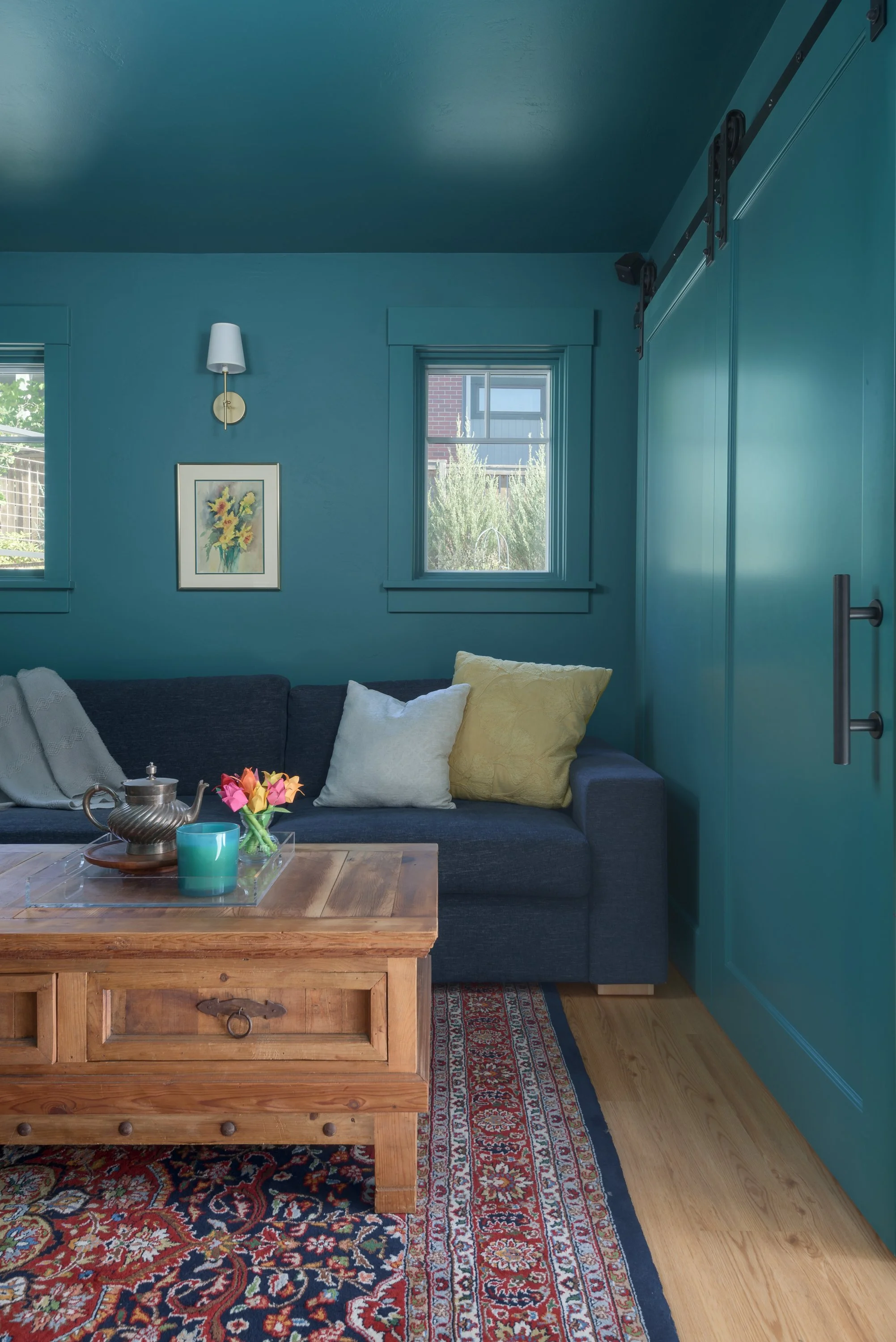 Movies and TV are enjoyed in a moody interior room, featuring dark green walls, a persian rug, wood coffee table, and comfy sectional sofa