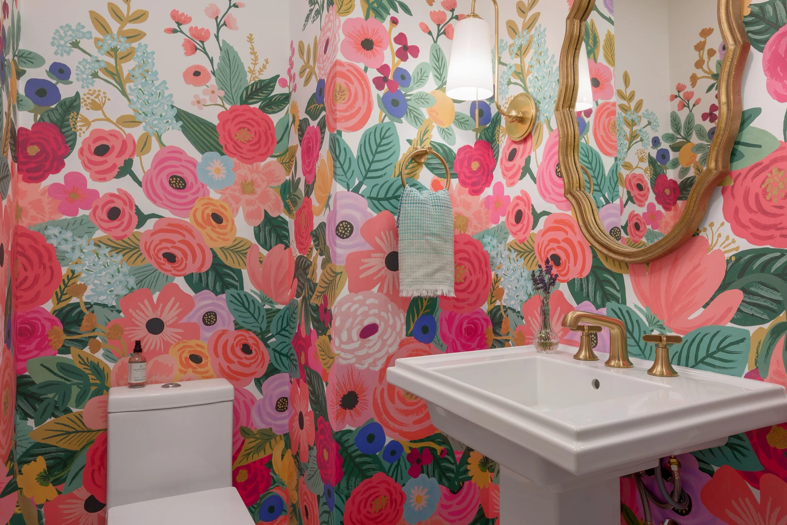 The downstairs half bathroom creates an immersive experience for guests with color drenching floral wallpaper