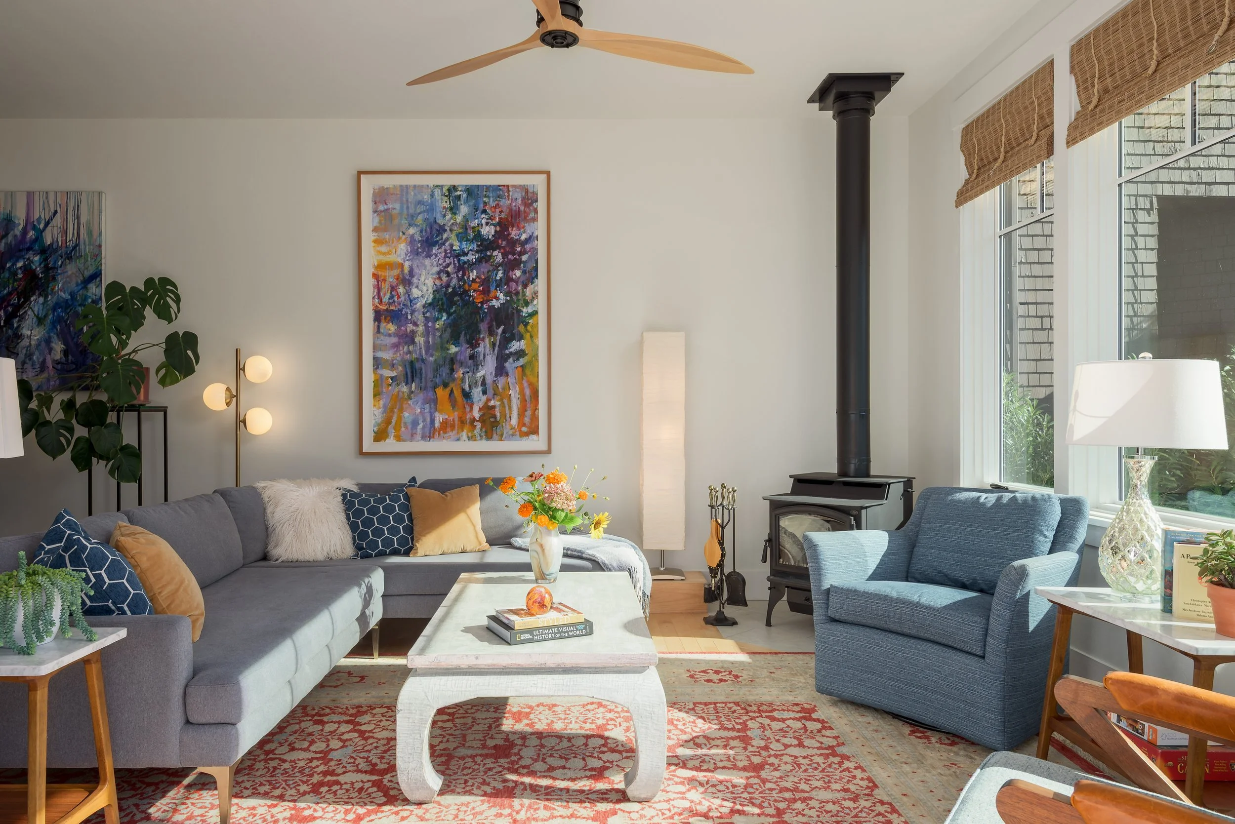 Large-scale art is a focal point of this living room, which is balanced with a neutral sectional sofa, ming-inspired coffee table, and blue reading chairs.