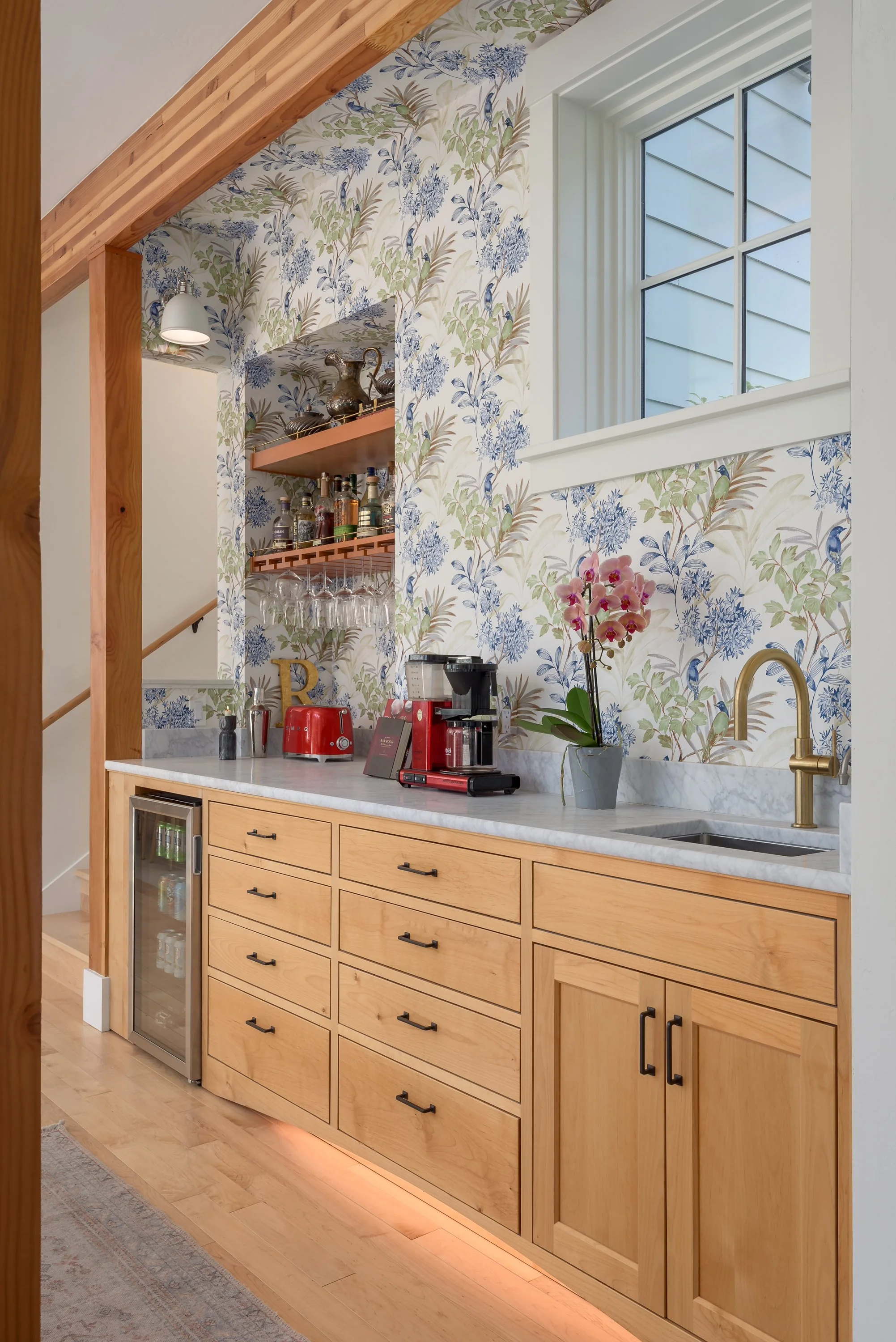 The wet bar and coffee station enjoys colorful yet refined wallpaper that injects fun personality