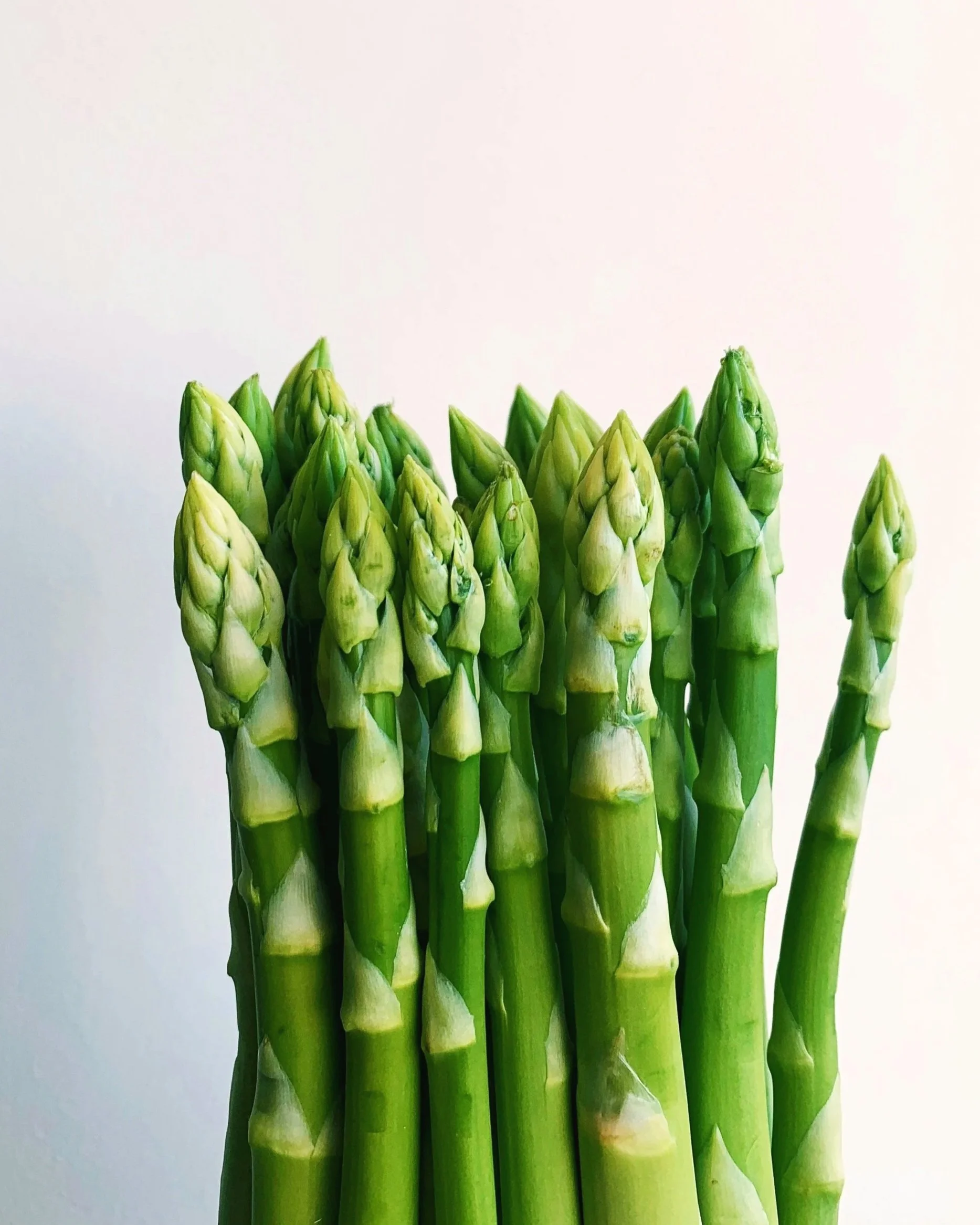 Close-up of fresh green asparagus spears against a plain light background.