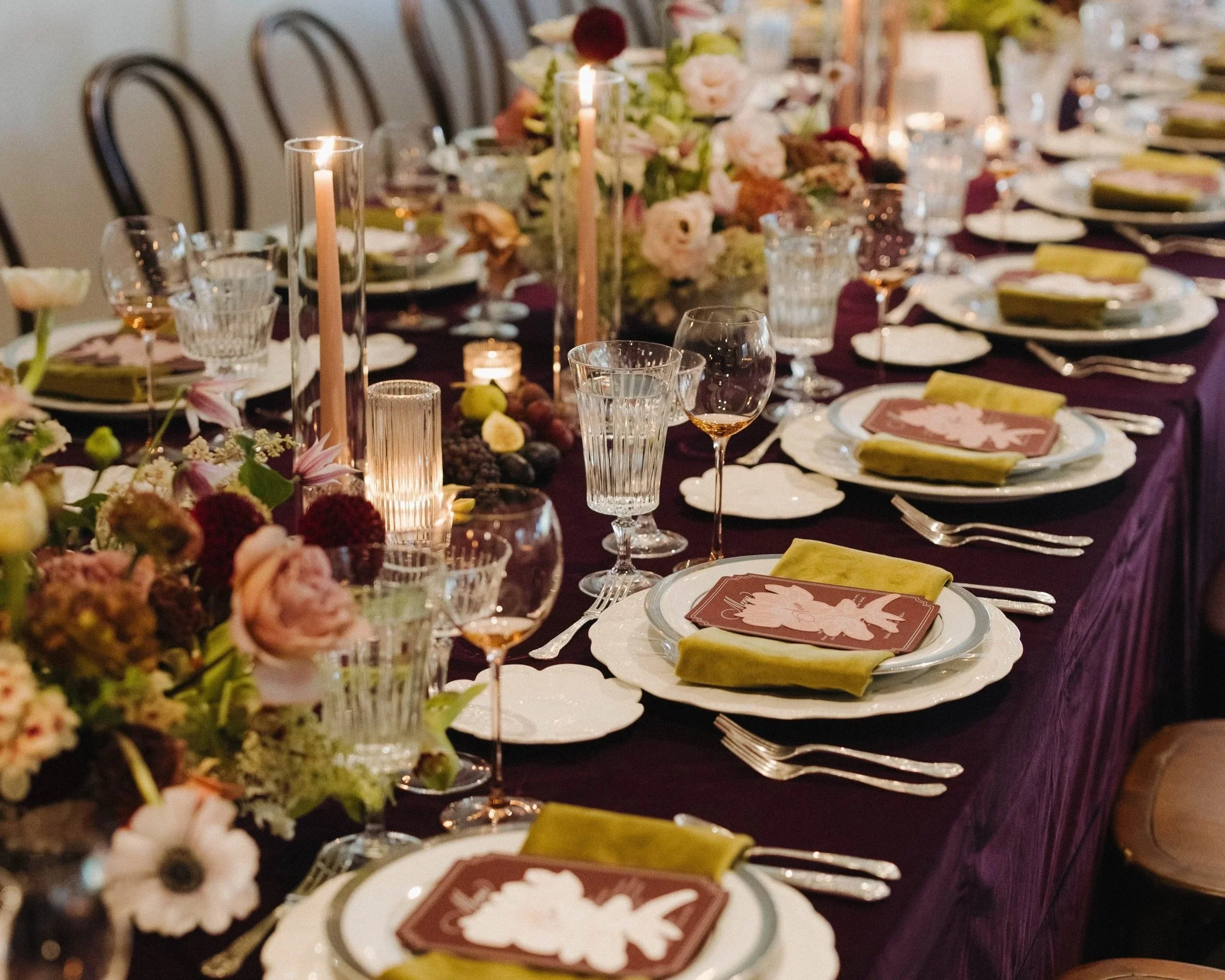 A long dining table set for a formal event with floral centerpieces, candles, glassware, and dinnerware.