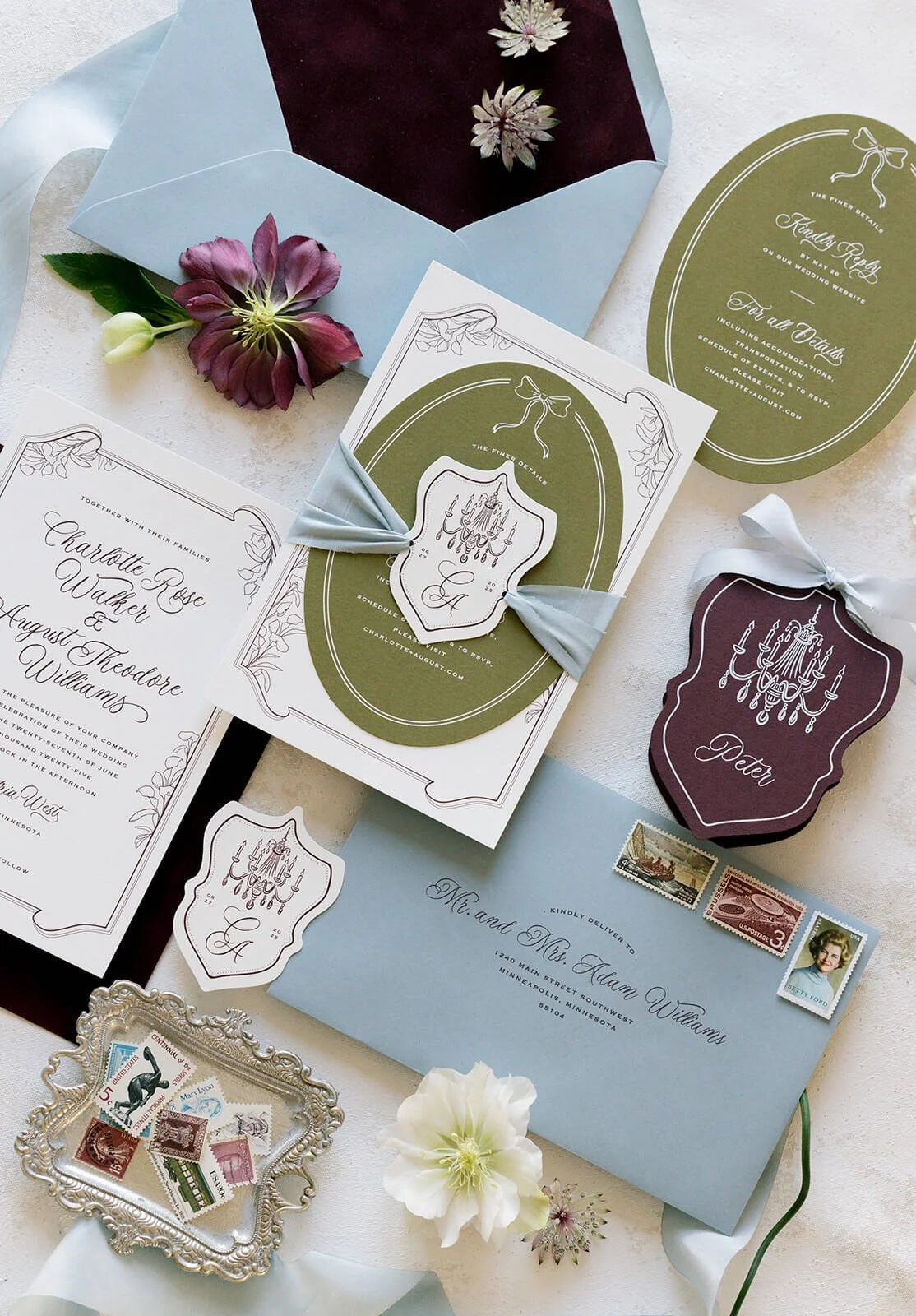 Wedding invitation suite with floral accents, stamps, and decorative tags on a white surface.