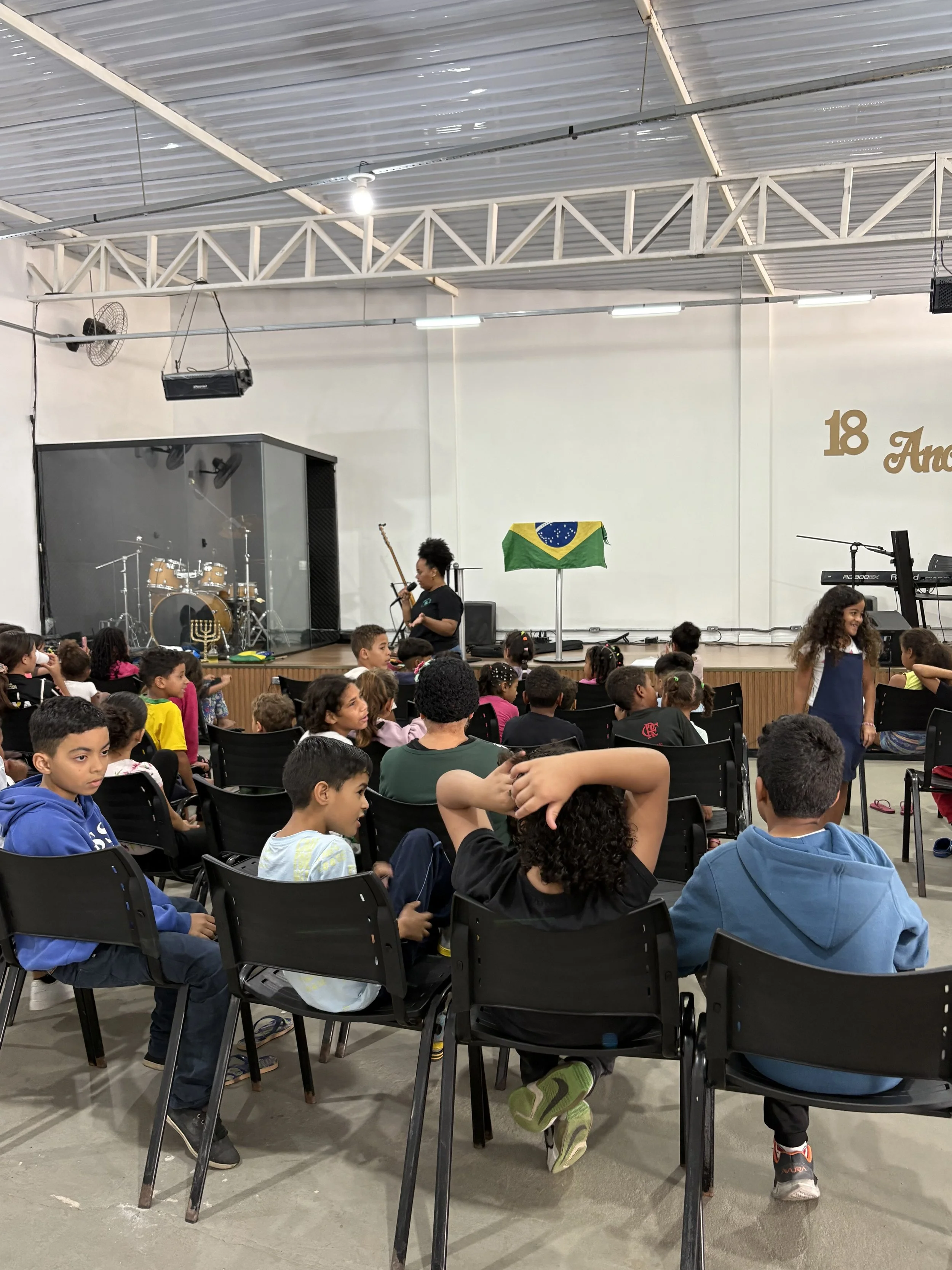 Lessons in Brazil on God's love as children are seated in a room filled with youth and adults.