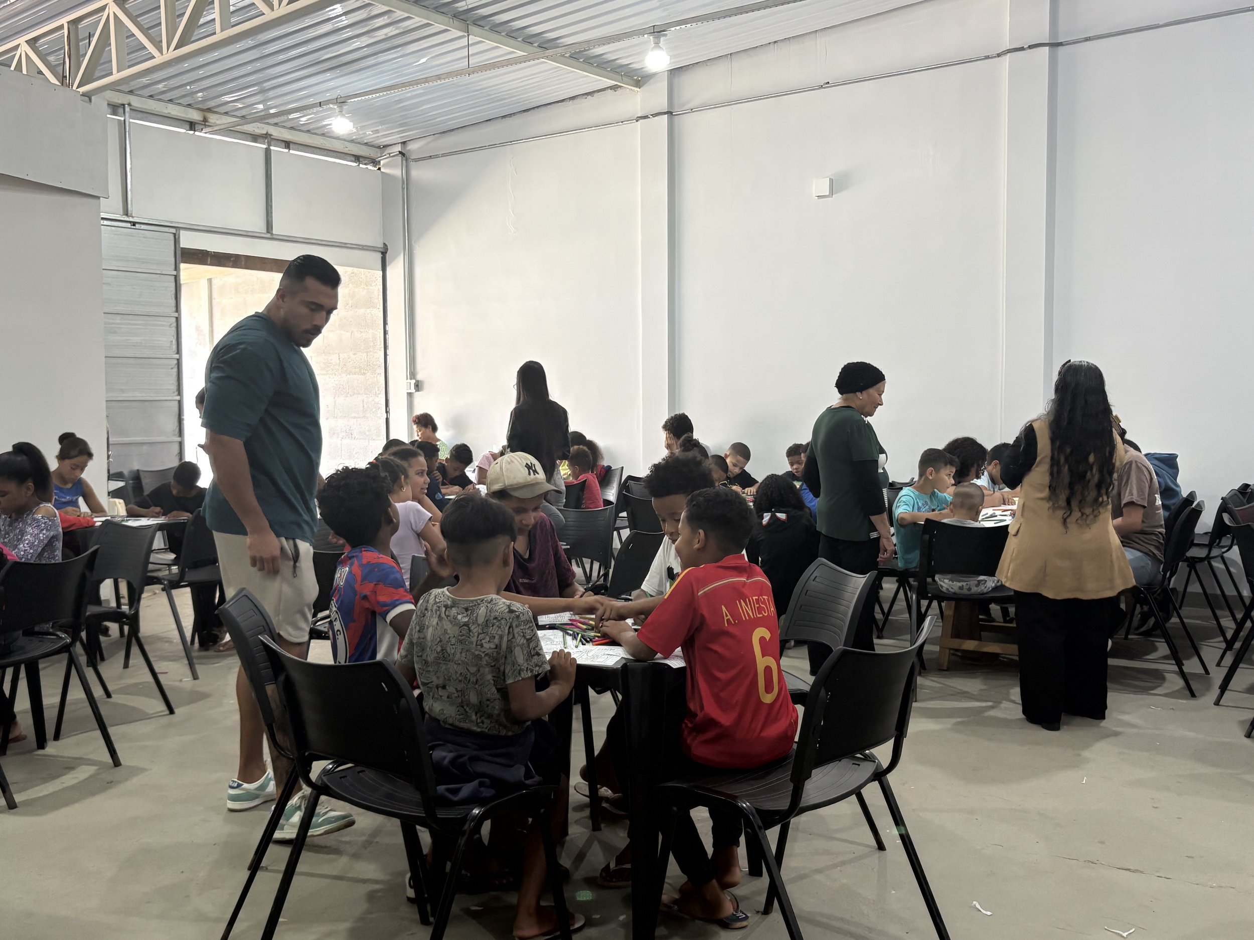 Children and adults in Brazil, sitting at tables playing and working on activities while teaching them about the love of Jesus, the Son of God.