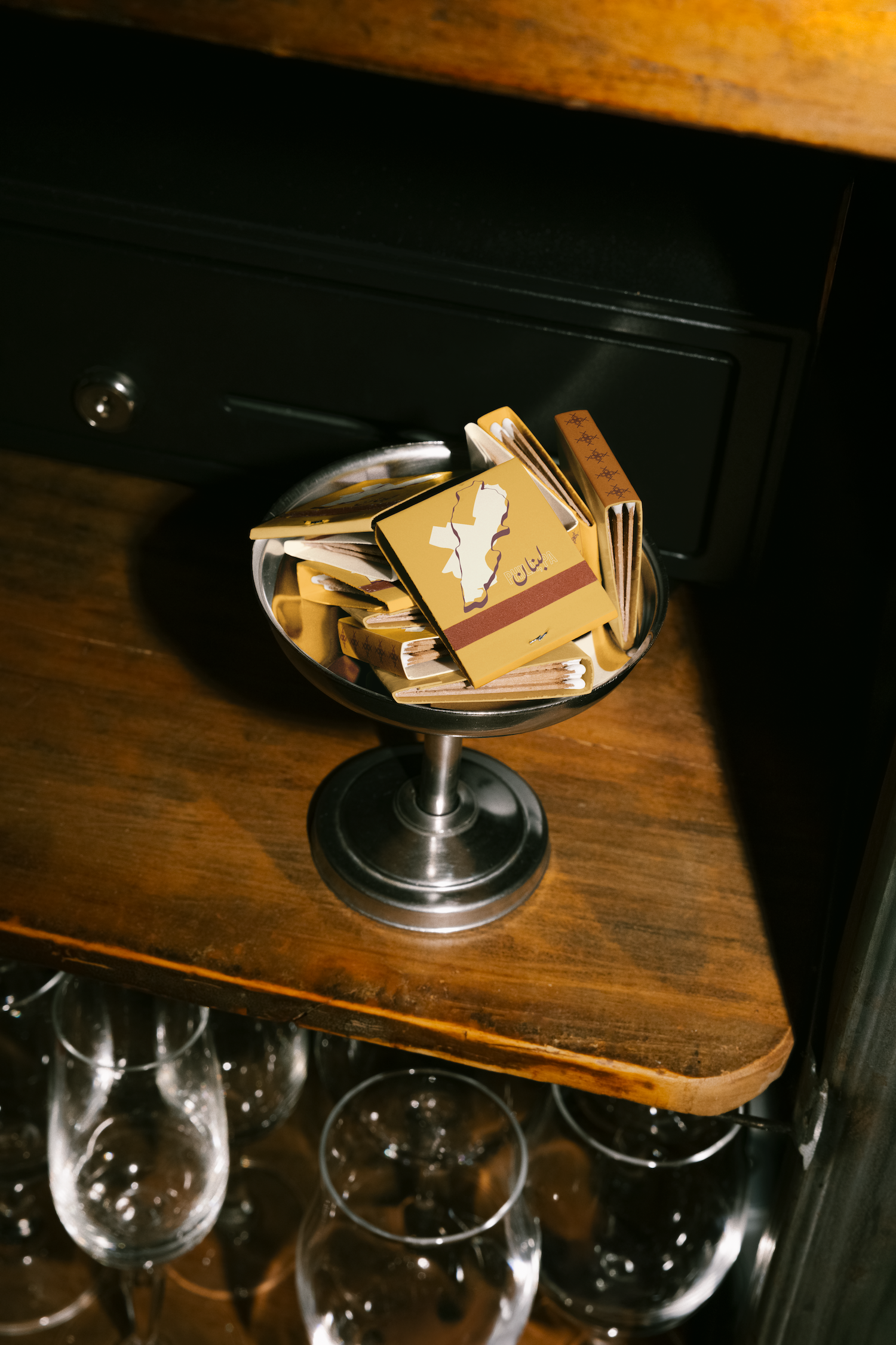 image of matchbooks in a silver ice cream bowl on a wooden shelf filled with glassware
