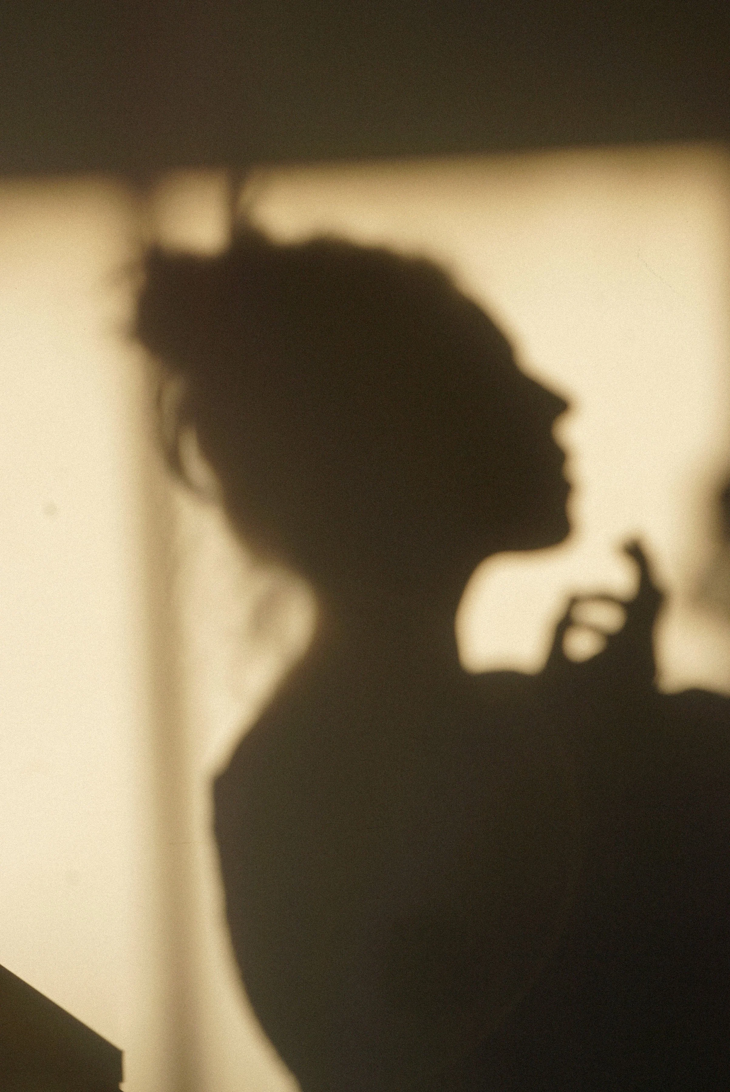Silhouette of a woman with hair in a bun, holding her hand close to her face in front of a light background.