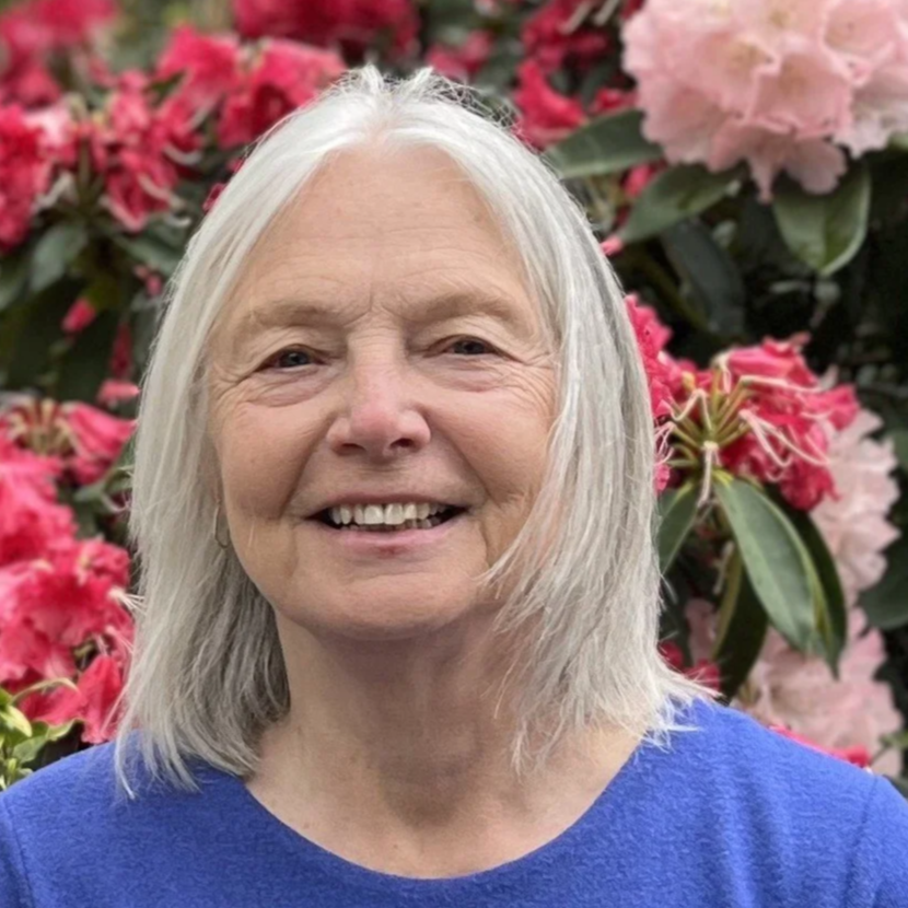 Photo of Vashon Heritage Museum's vice president, Susan Martin, standing outside in front of pink flowering rhododendrons.