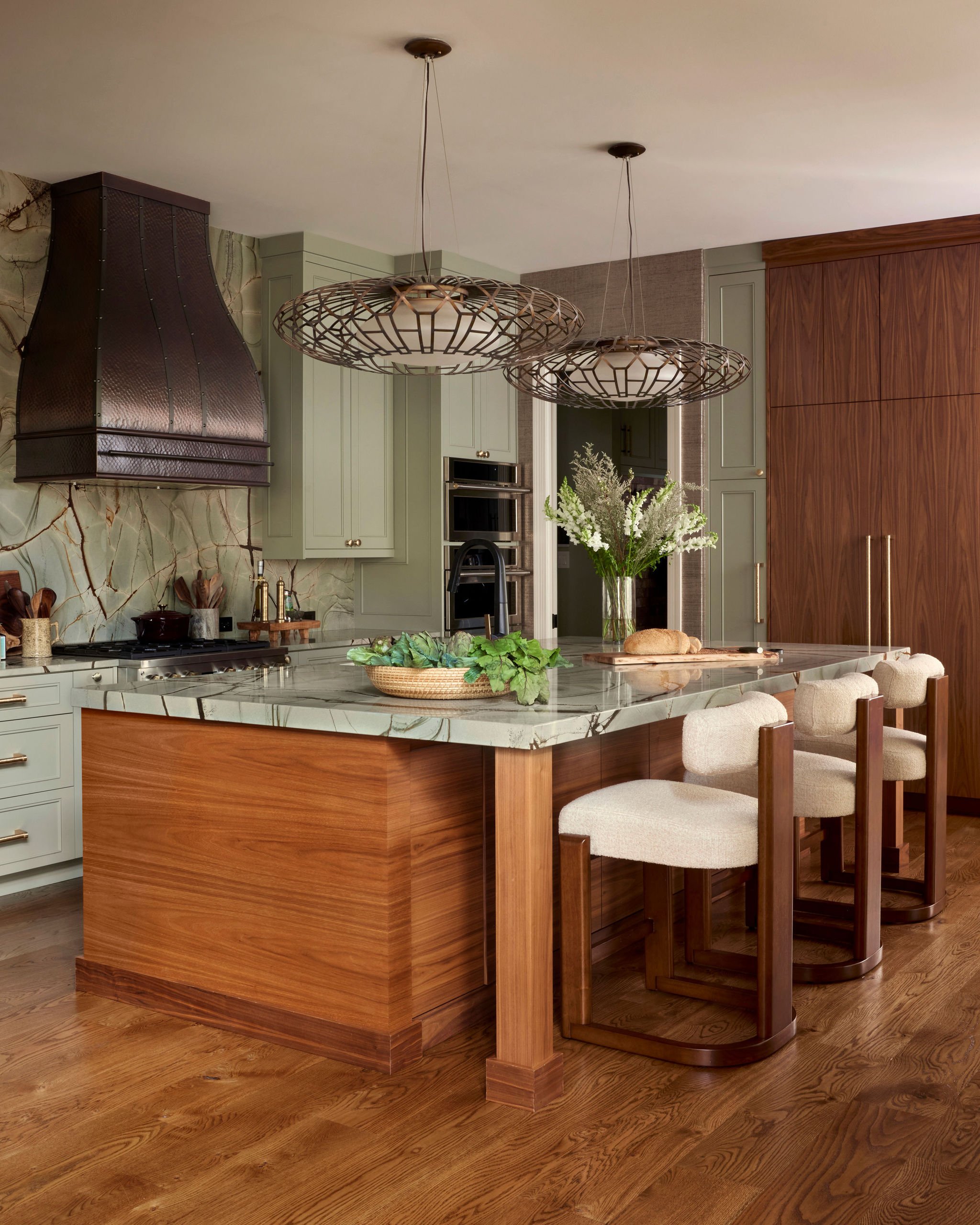 A modern kitchen with a marble island, green cabinets, wooden accents, and hanging woven light fixtures.