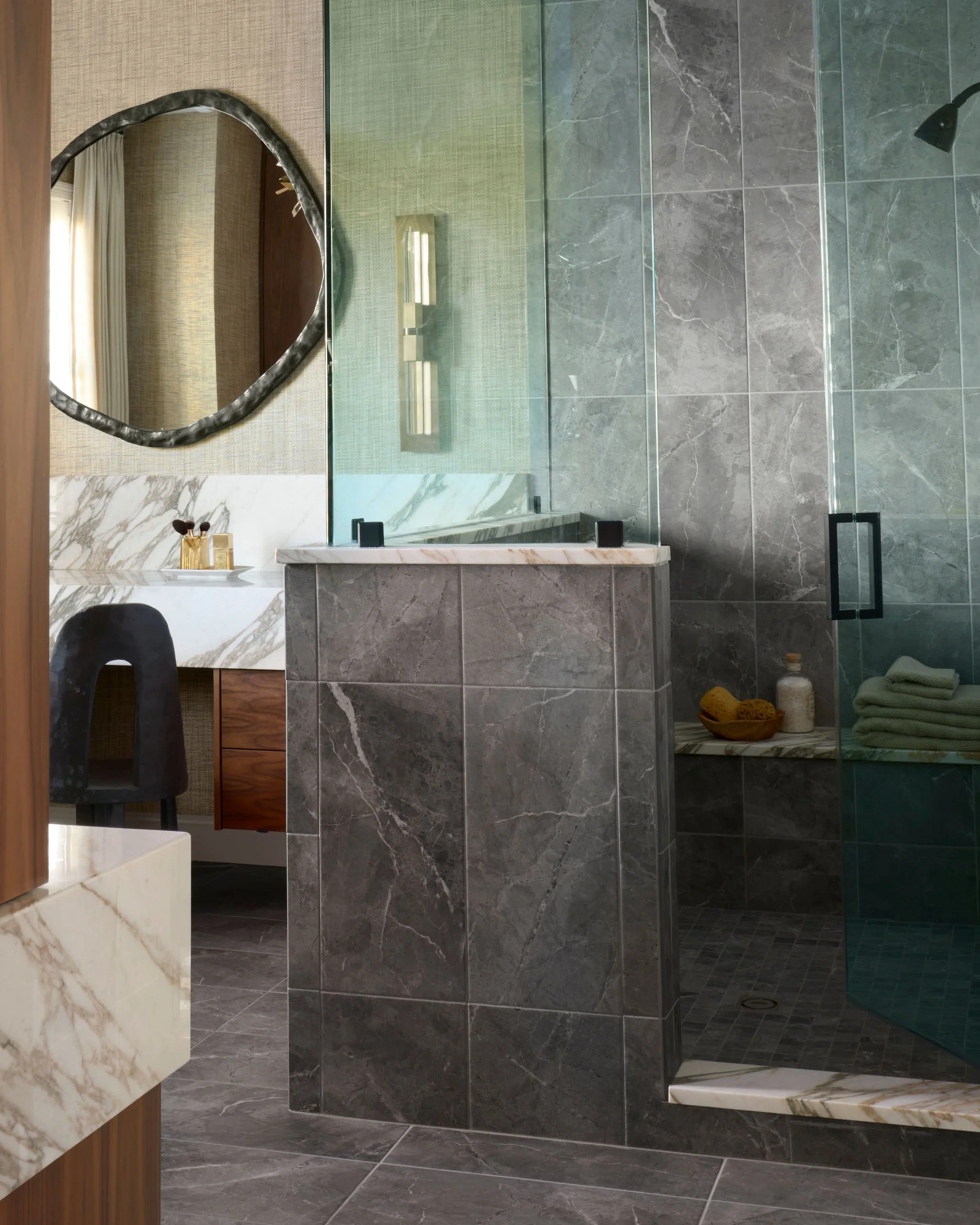 Modern bathroom featuring gray marble tiles, a glass shower enclosure, a white marble vanity top, and a large mirror with a decorative black frame.