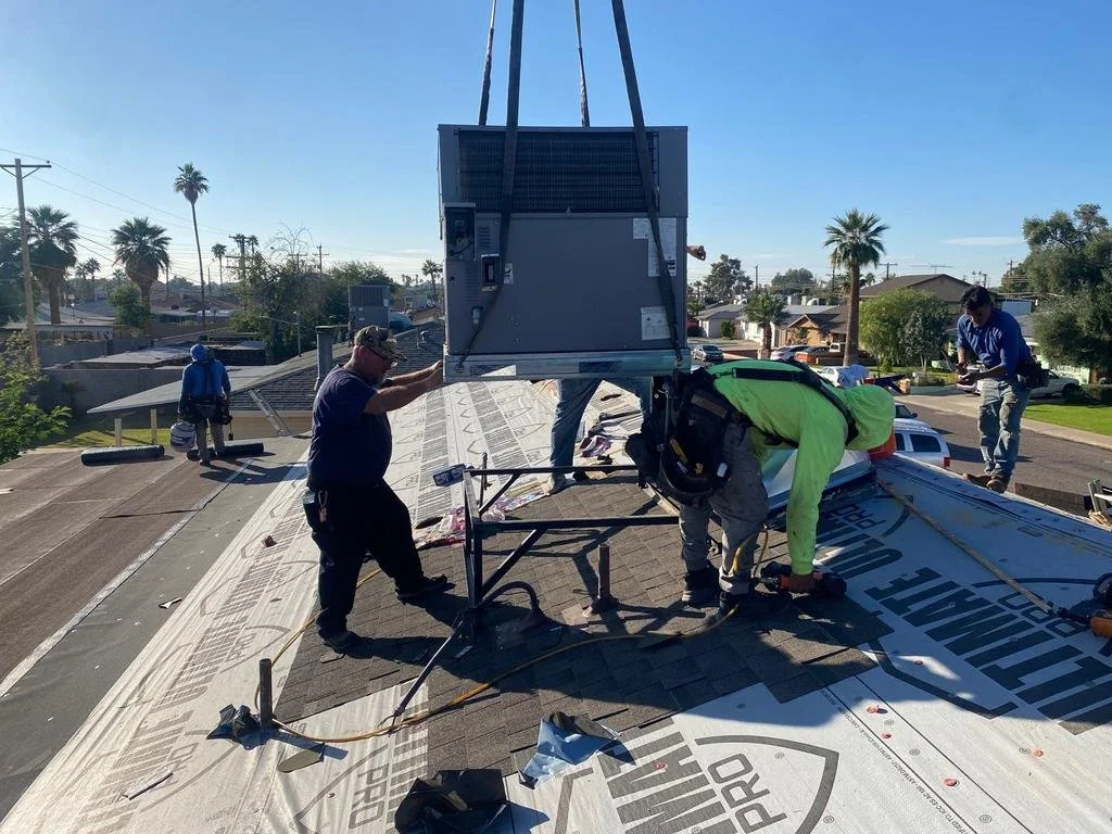 Workers install HVAC equipment on a residential roof during daytime, with palm trees and houses in the background.