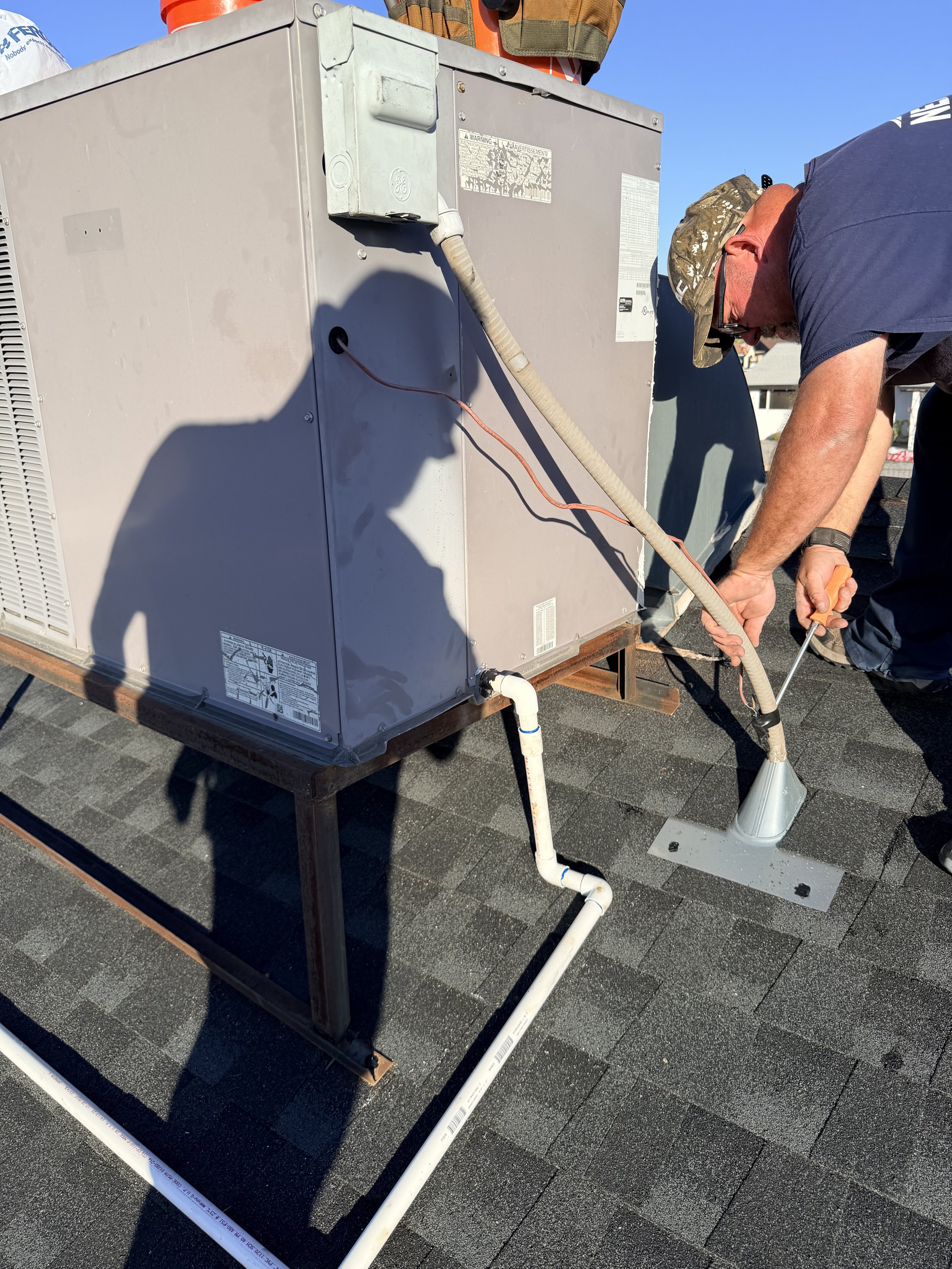 Technician working on HVAC unit on a rooftop, connecting or inspecting pipes and ducts.