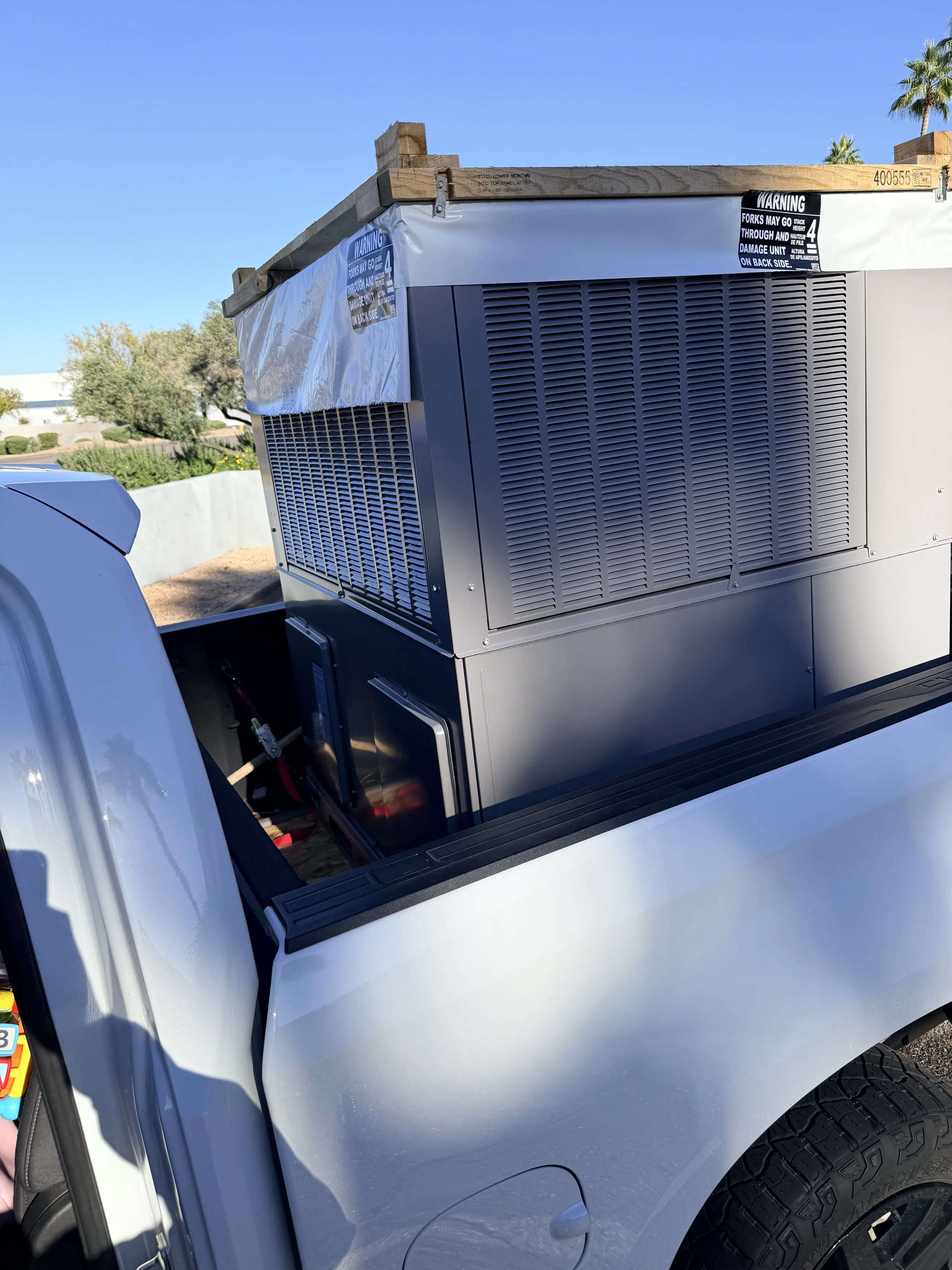 A large industrial or commercial air conditioning unit installed in the bed of a pickup truck with palm trees in the background.