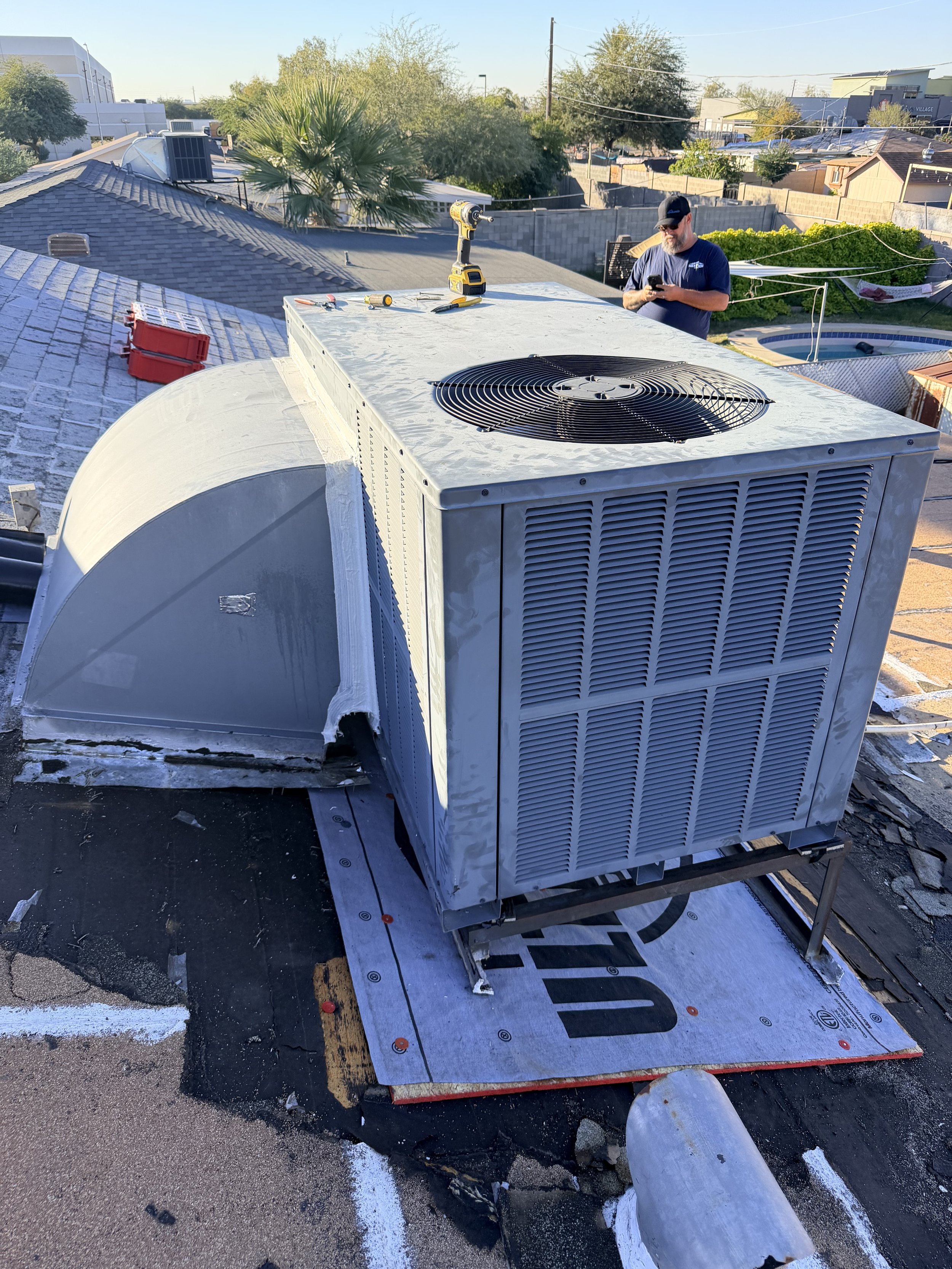 A HVAC unit on a rooftop with a technician working in the background, surrounded by residential buildings and trees.