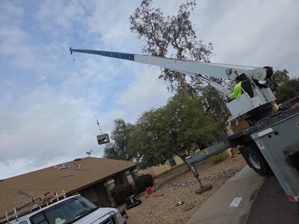 A crane lifting a small house on the roof of a larger building in a suburban neighborhood.