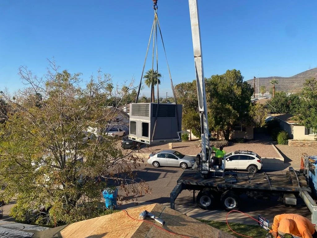 A crane lifting a window air conditioning unit onto a building.