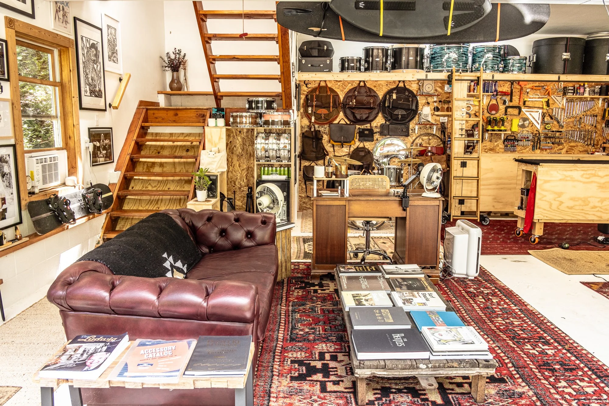 A well-organized workshop with woodwork and musical equipment, featuring a vintage leather sofa, stacks of books, a workbench with tools, and wall-mounted guitars and supplies.