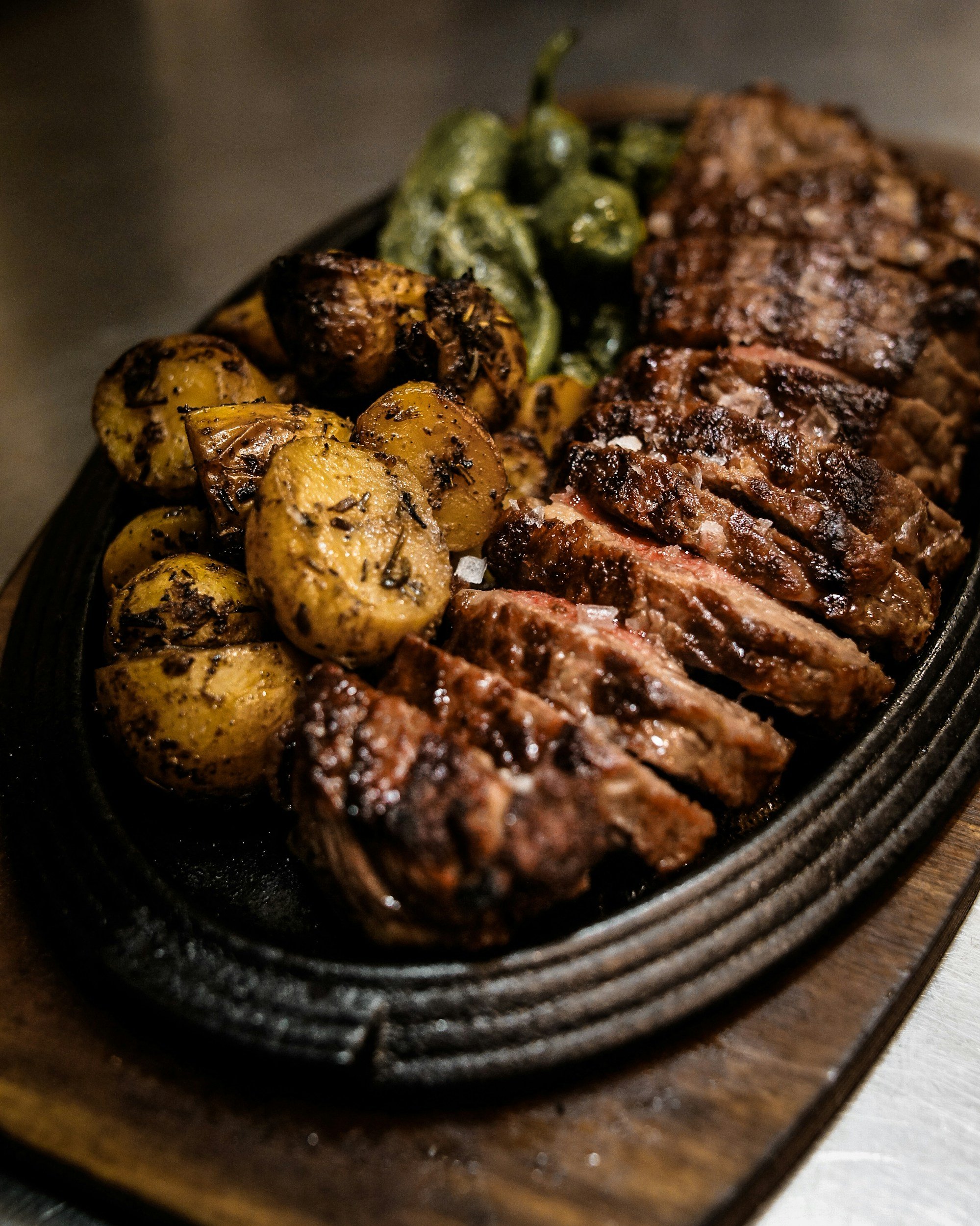Steak with grilled roasted potatoes and roasted jalapeño peppers on a sizzling cast iron platter.