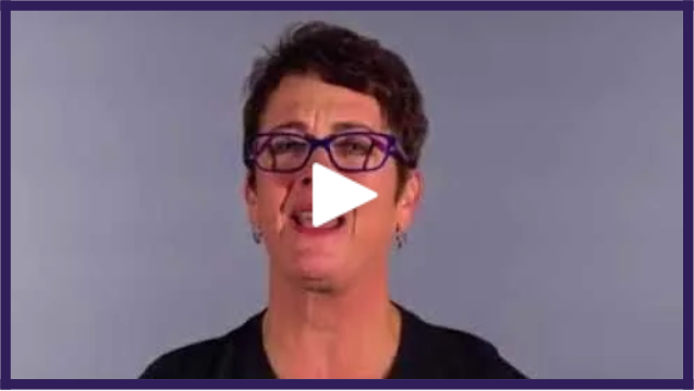 A woman with short dark hair, wearing glasses and earrings, standing against a purple background, speaking or smiling at the camera.
