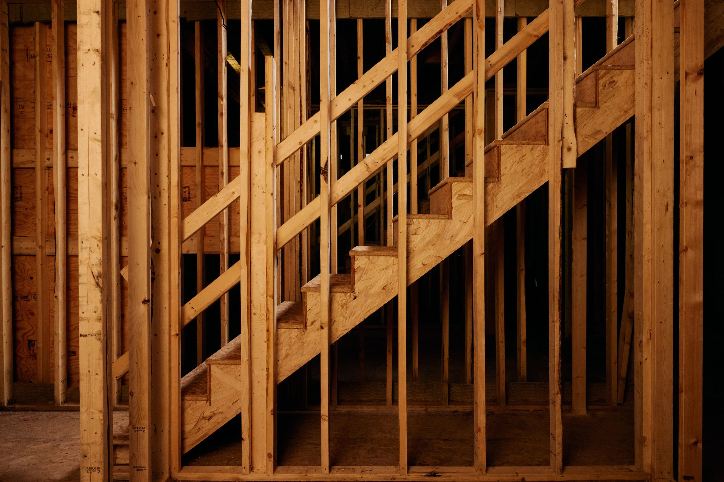 Interior view of a wooden staircase framed within construction wooden studs in a building under construction.