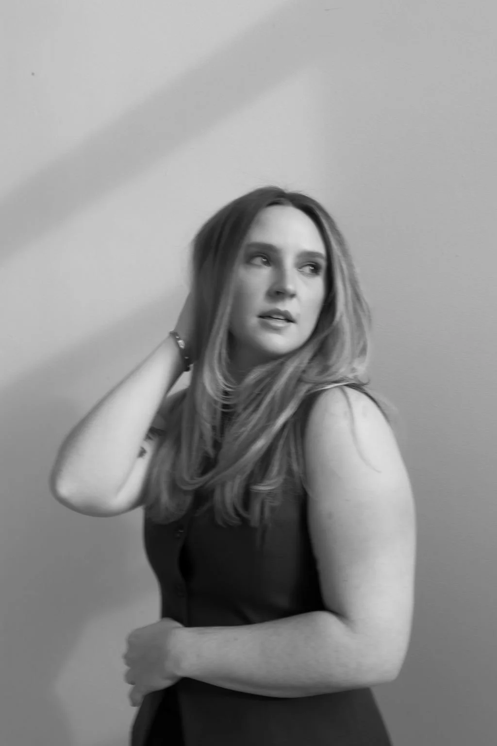 Monica Renee Netzel, a Chicago based luxury hairstylist and blonde specialist looking off to the side with her hand in her hair.