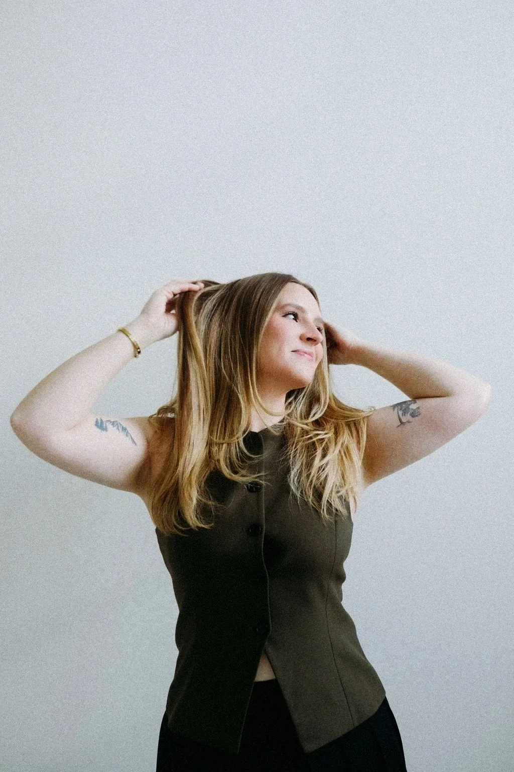 Monica Renee Netzel, the best blonde specialist and hairstylist in Chicago, standing with her arms raised over her head with hands in her hair. She has a happy smile on her face.