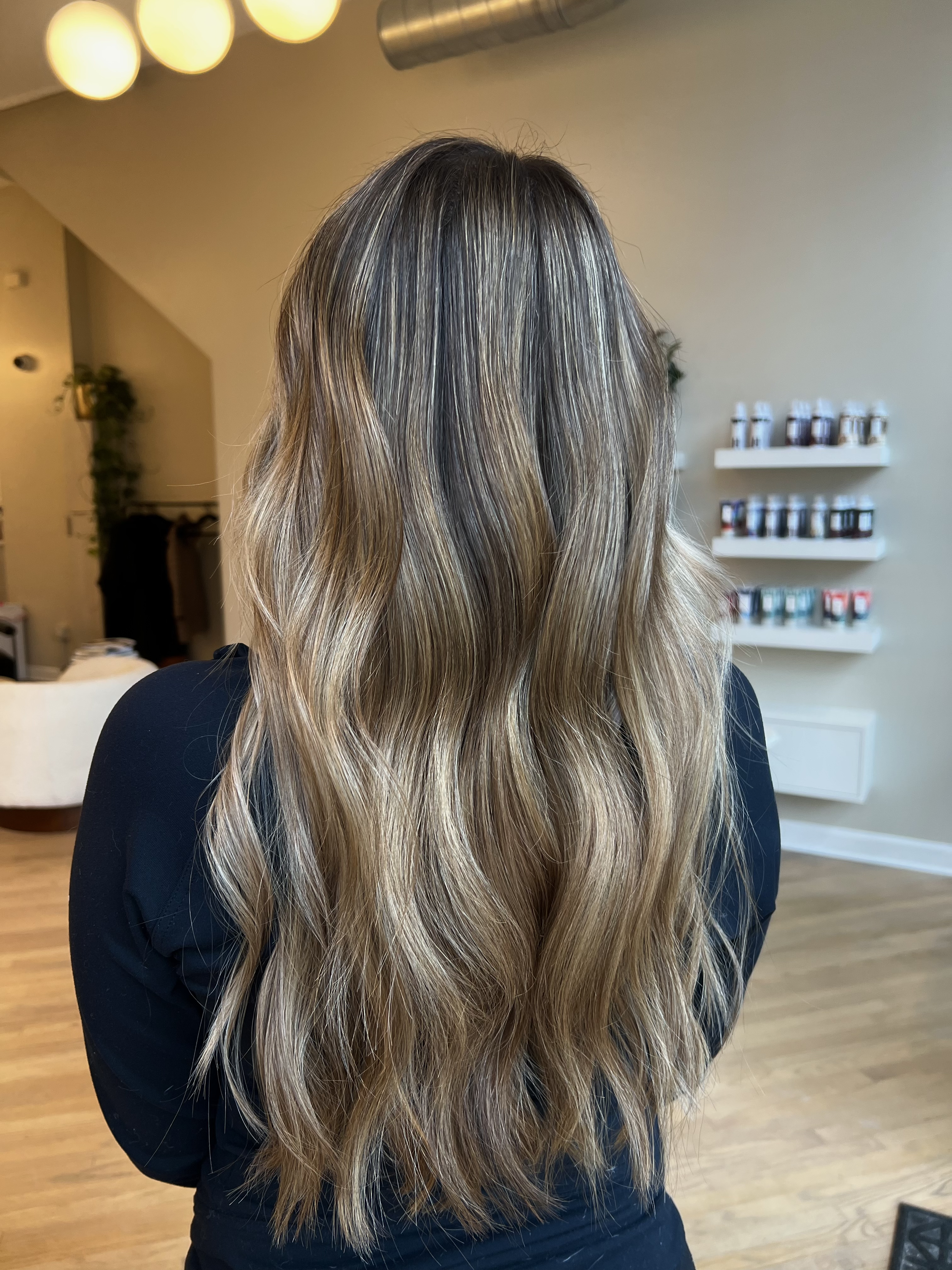Back view of a woman with long, wavy, blonde hair in a salon, color and style by Monica Renee.