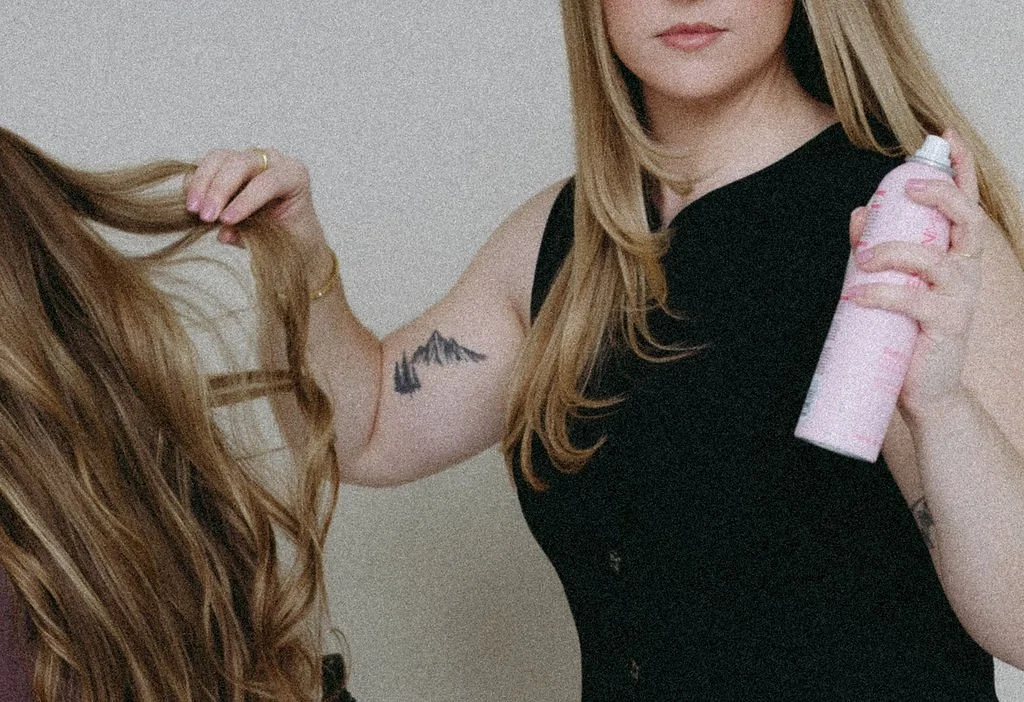 Monica Renee Netzel luxury and celebrity  Chicago hairstylist and blonde specialist holding a bottle of hairspray in one hand and holding a the client hair in the other hand.