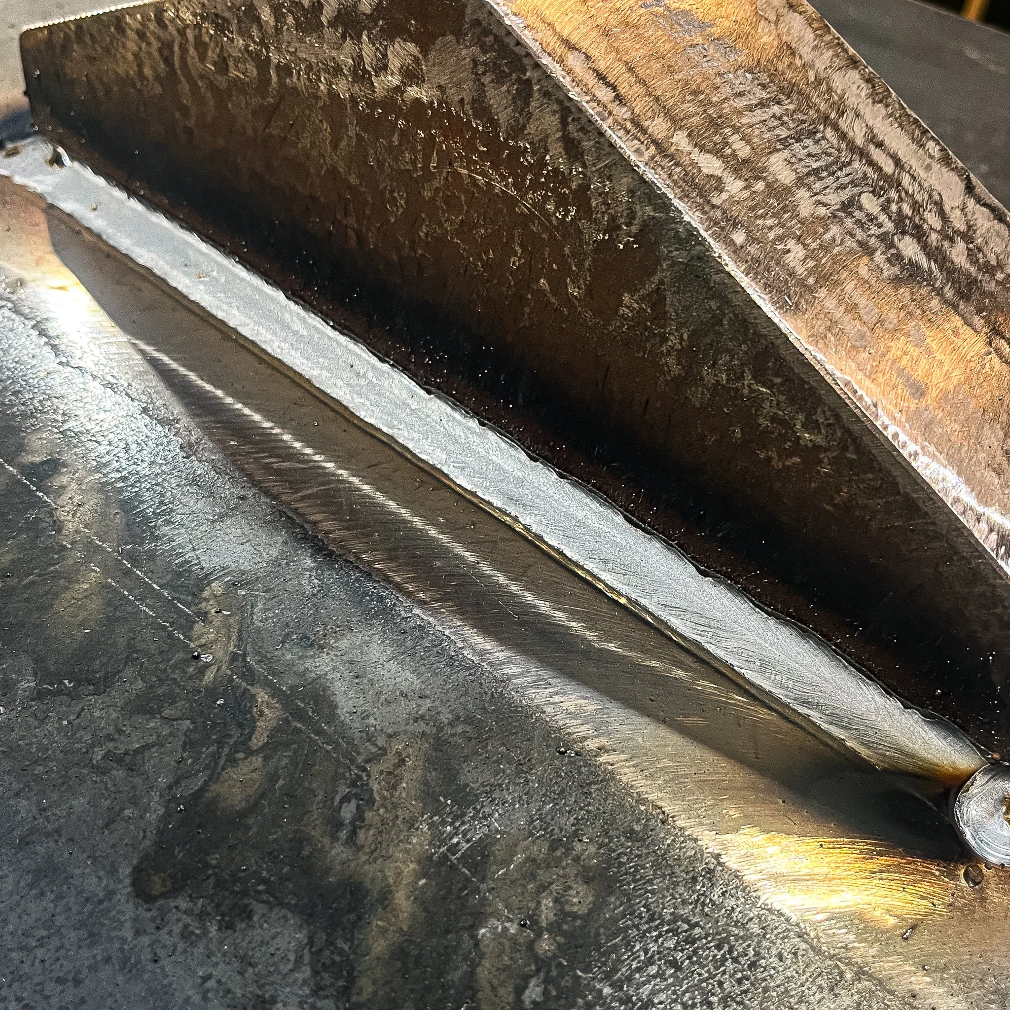 A metal surface with a cut or weld seam, showing signs of heat and oxidation, with a rough and smooth textured metal piece placed on top.