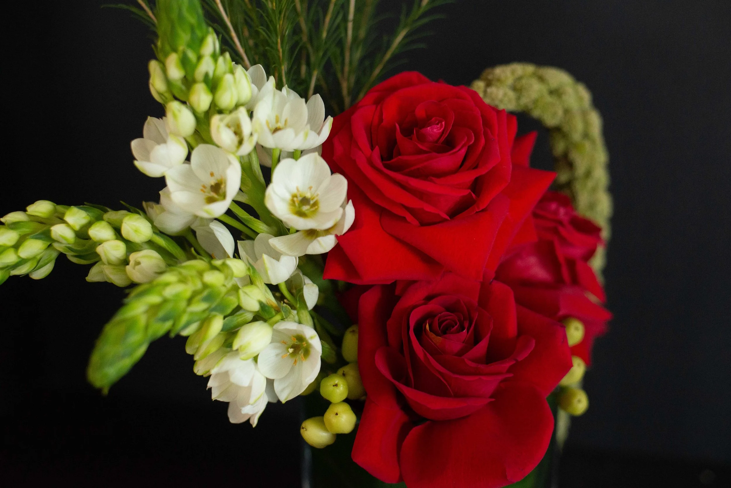 A bouquet of roses, white flowers, and greenery on a black background.
