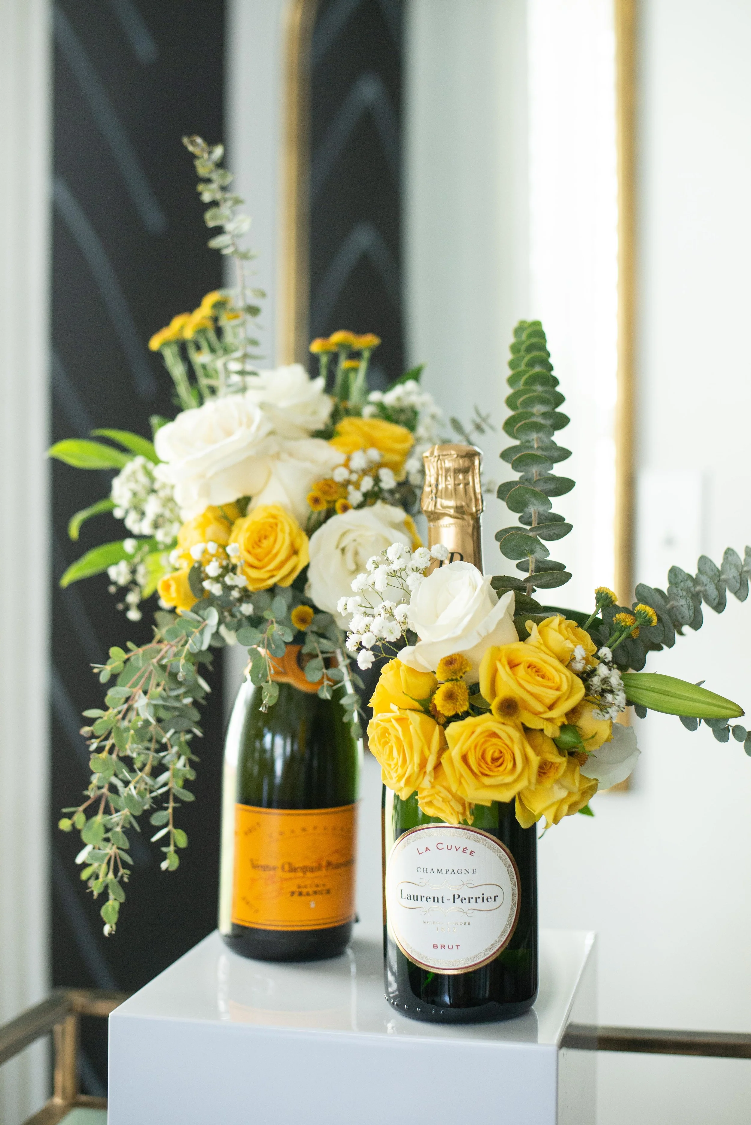 Two bottles of champagne with floral arrangements on a white table.