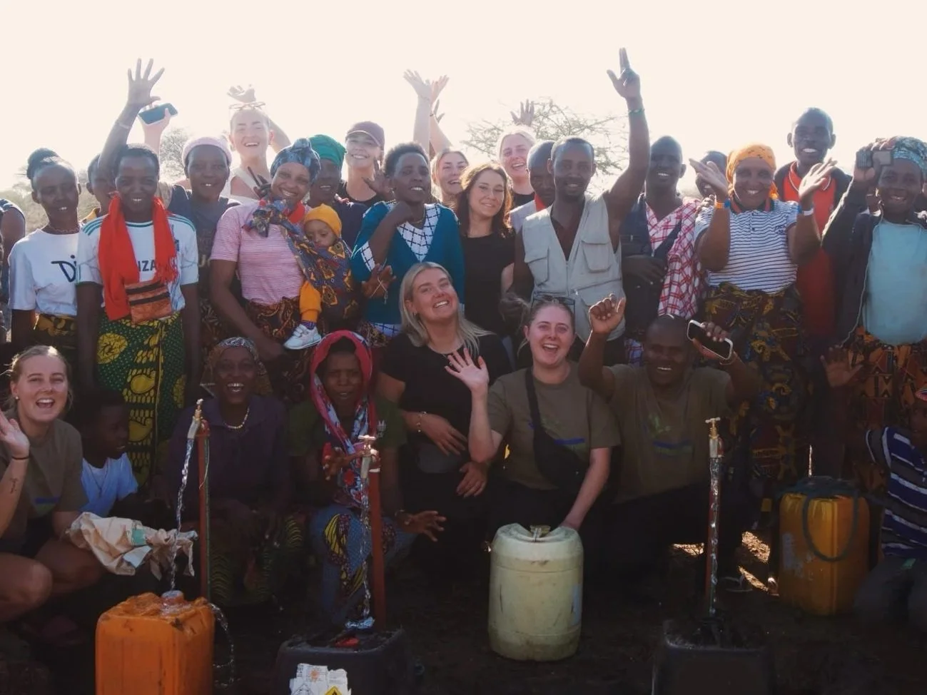 En grupp människor med glada ansikten, some blandade med lokalbefolkningen, tillsammans på utomhusområde.