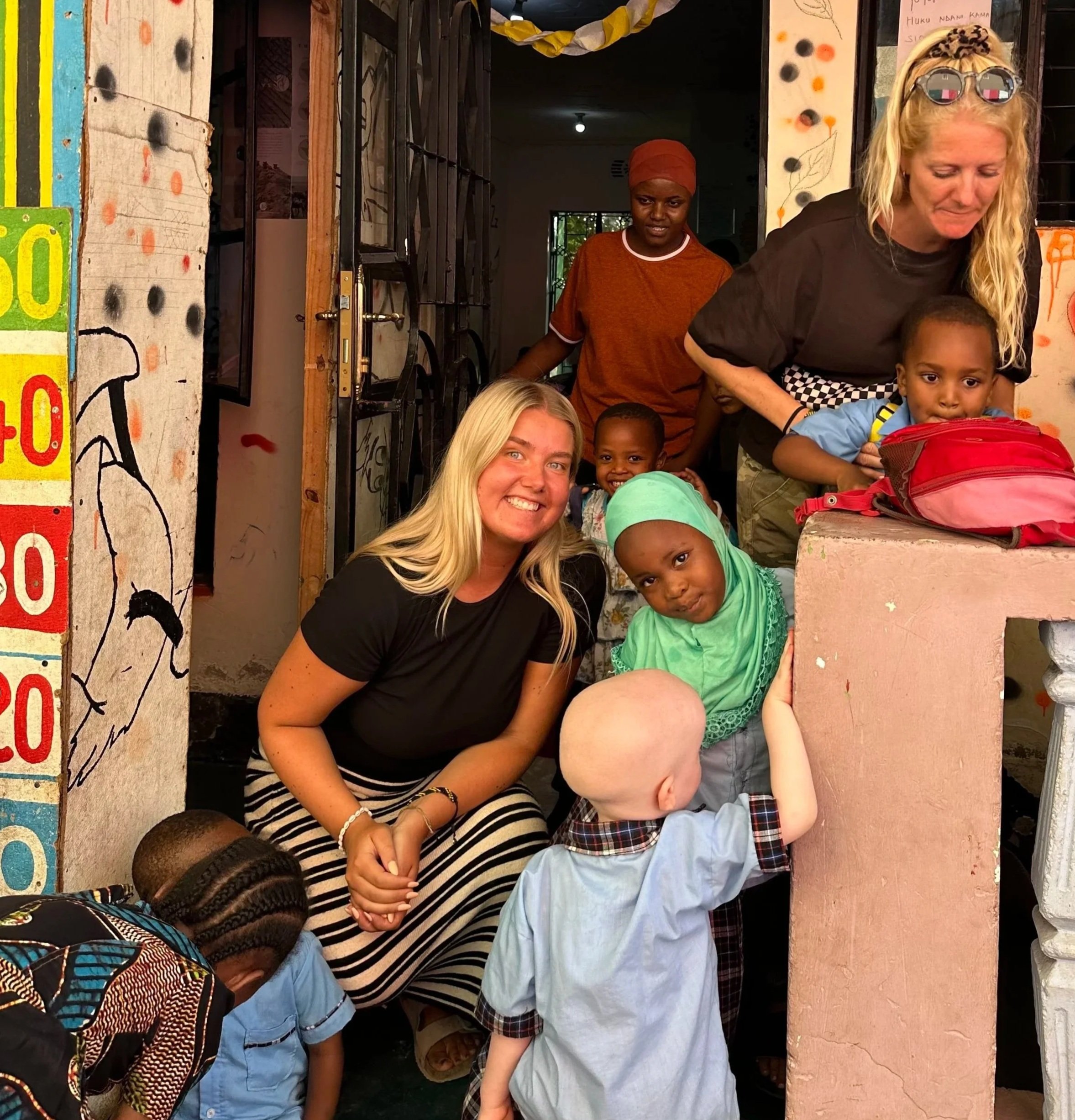 En grupp vuxna och barn utanför en byggnad, flera av barnen tittar mot kameran och det är ett glatt samtalsklimat.