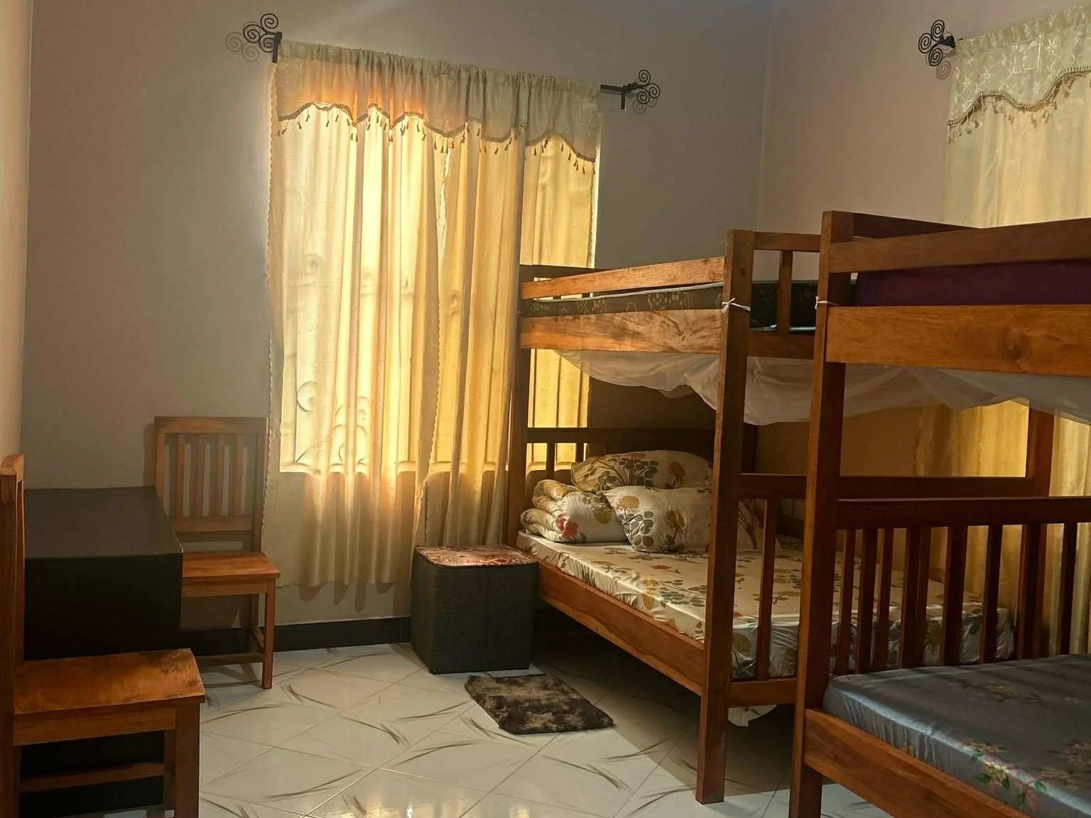 Ett sovrum med tre våningssängar, ett fönster med gula gardiner, och ett skrivbord med stol.