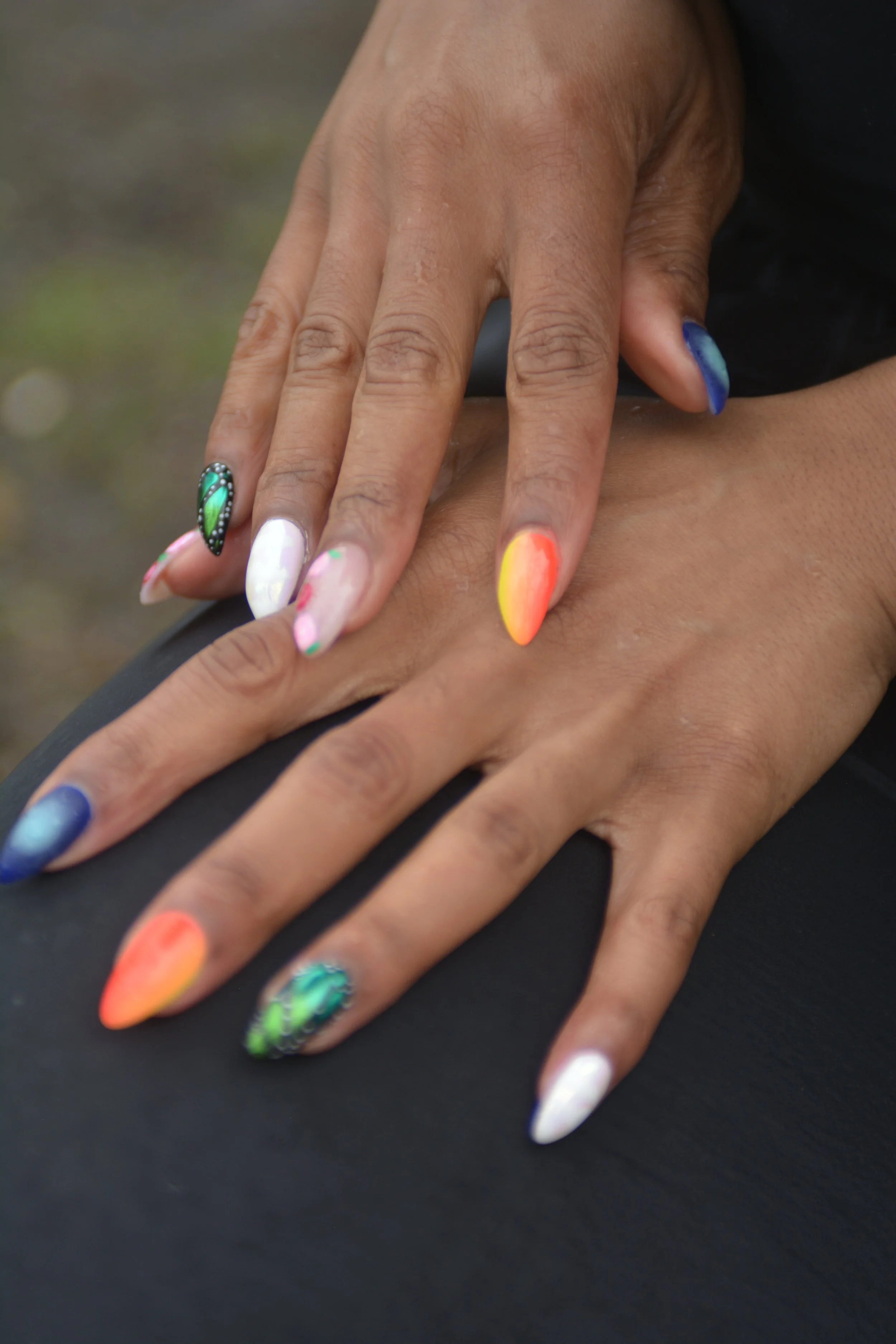 Close-up of hands with colorful and decorated nails against a dark background.