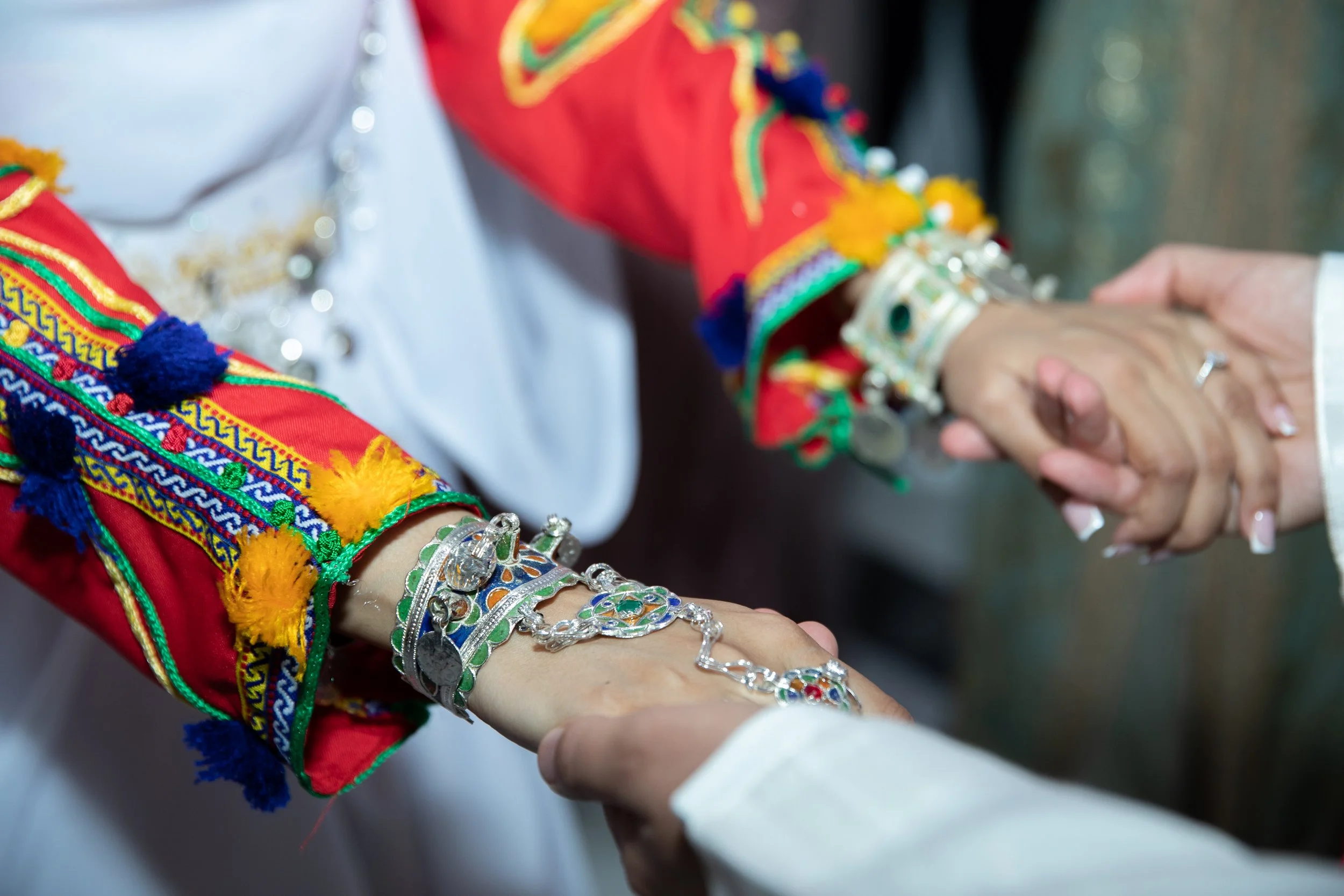 Two people holding hands during a ceremonial exchange, wearing colorful, embroidered traditional clothing and jewelry.