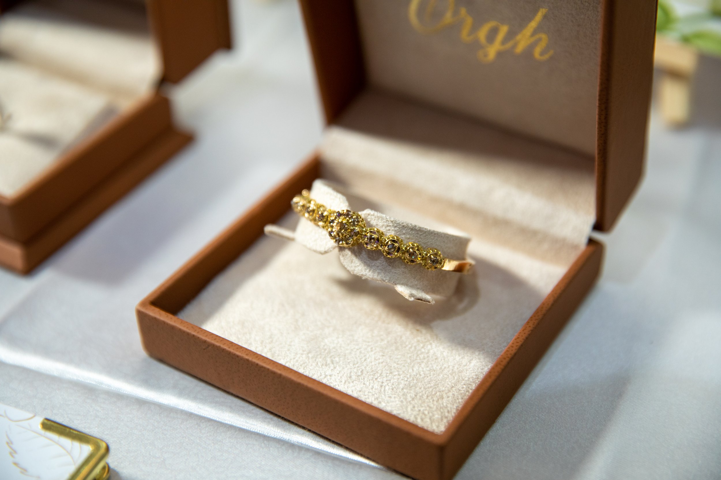A gold bracelet with yellow gemstones inside a brown jewelry box lined with cream-colored fabric.