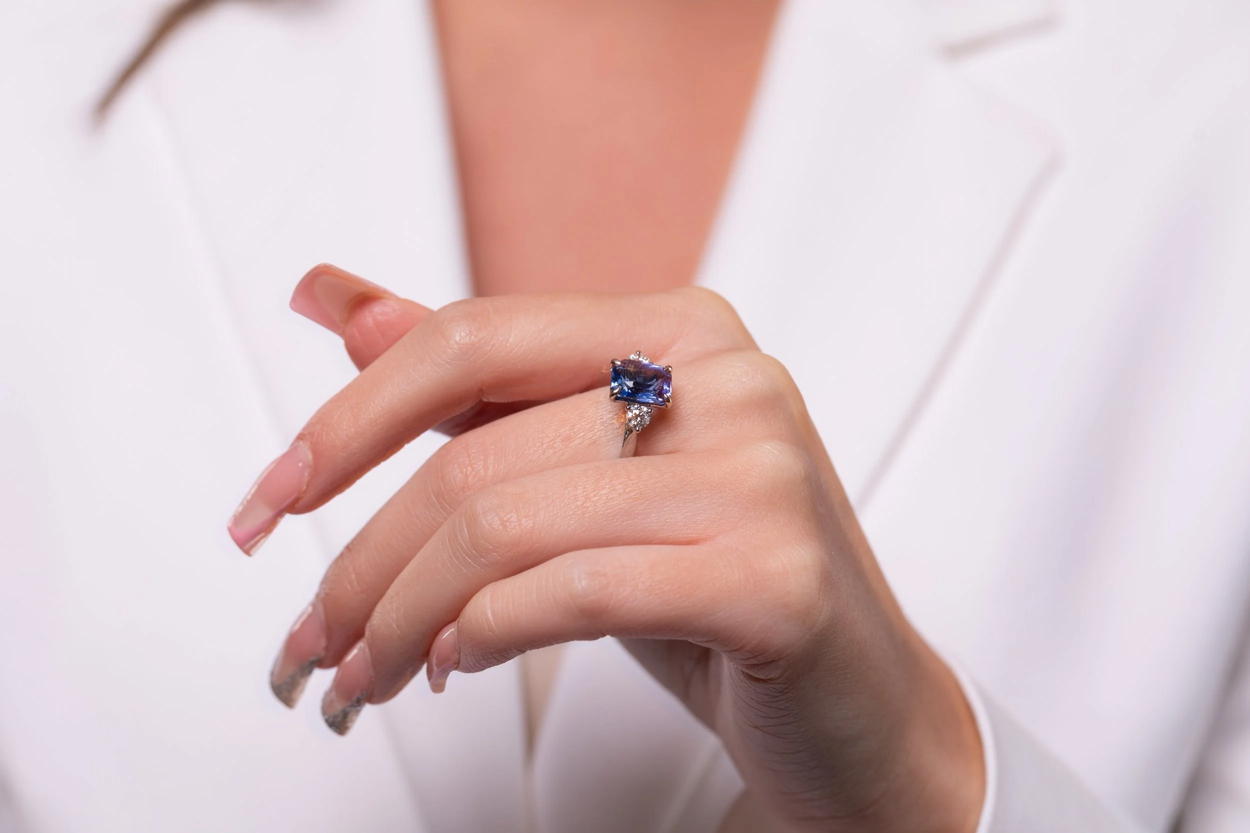 Close-up of a woman's hand with a large blue gemstone ring on her ring finger, wearing a white blazer.