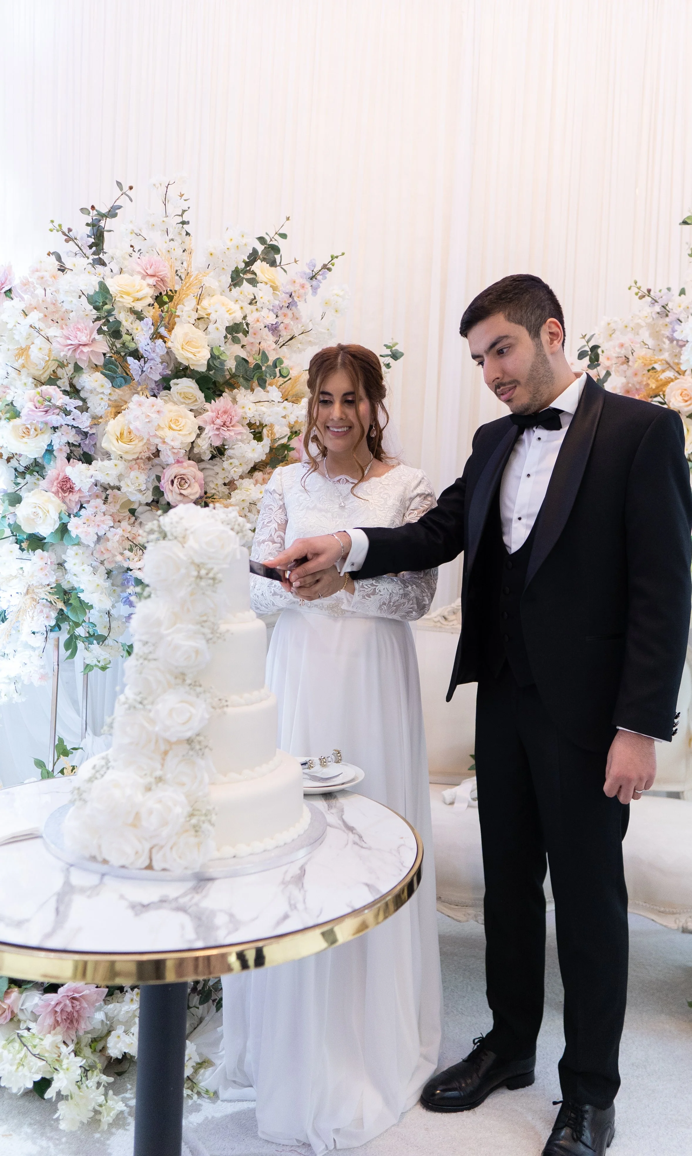 A bride and groom cutting a wedding cake surrounded by floral decorations.