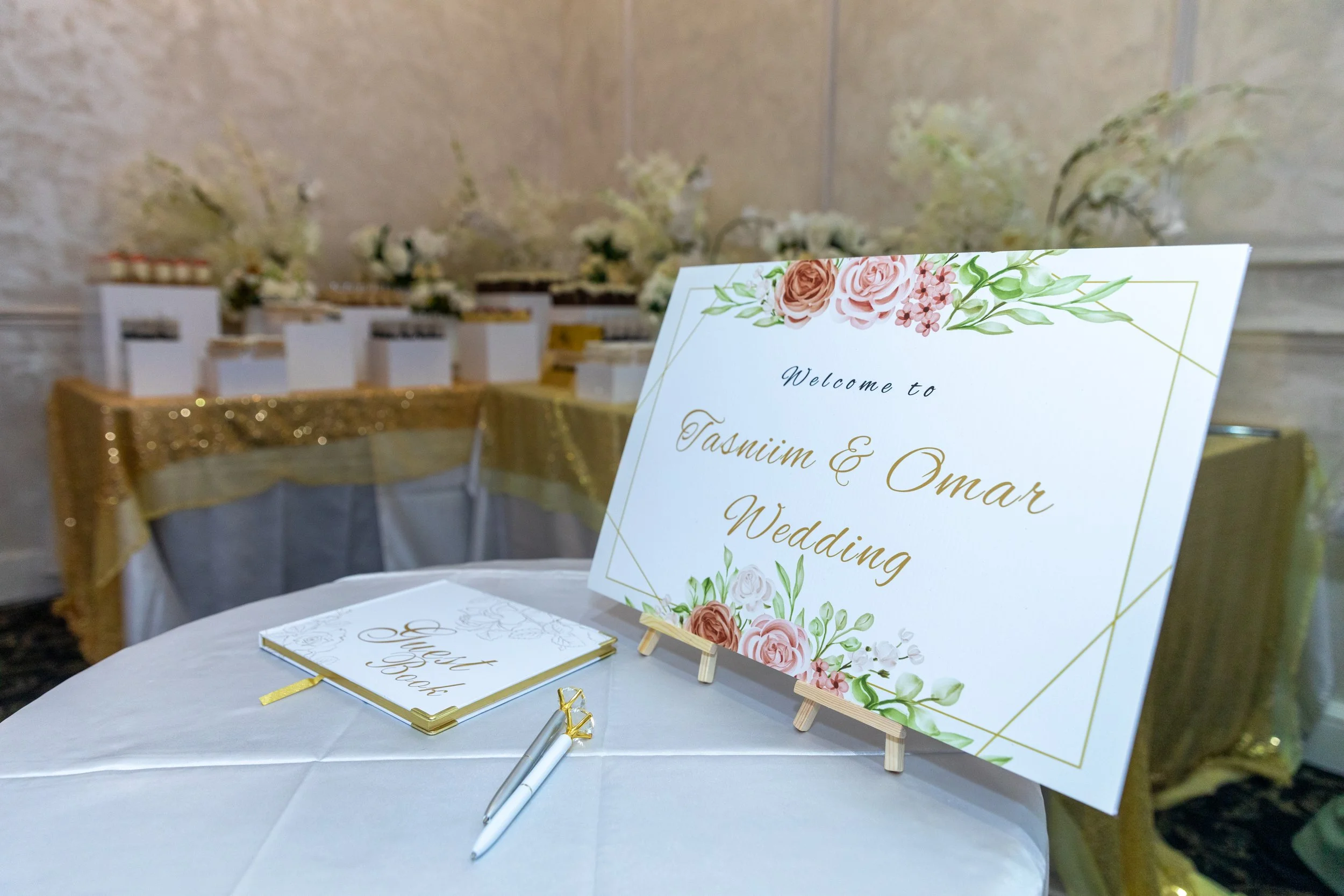 Wedding welcome sign with floral decoration and an guest book on a white table at a wedding reception.
