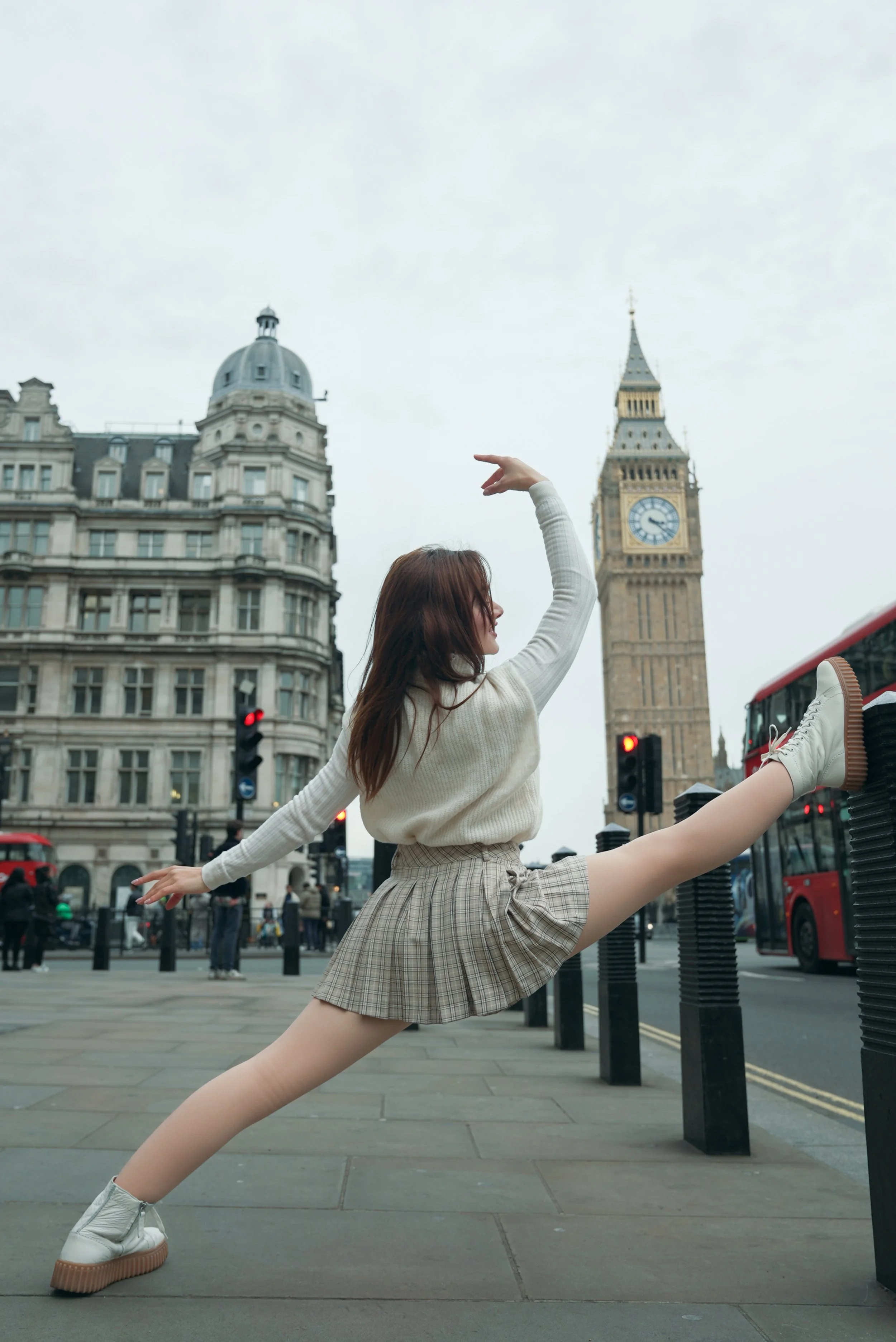 Woman in plaid skirt and white sweater stretching on a city sidewalk with Big Ben in the background.