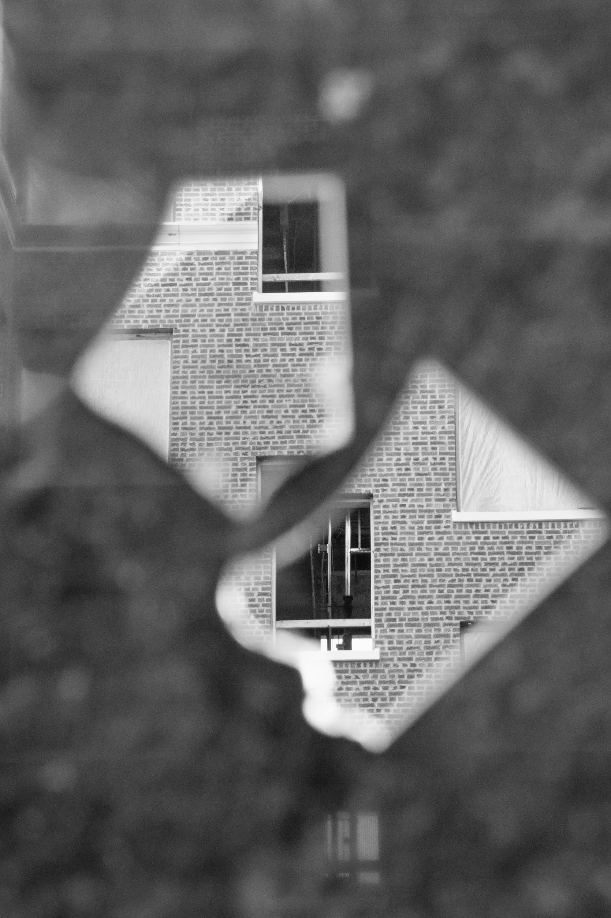 View of a brick building through a decorative metal fence with a geometric pattern, multiple floors, windows, and balconies in the background.