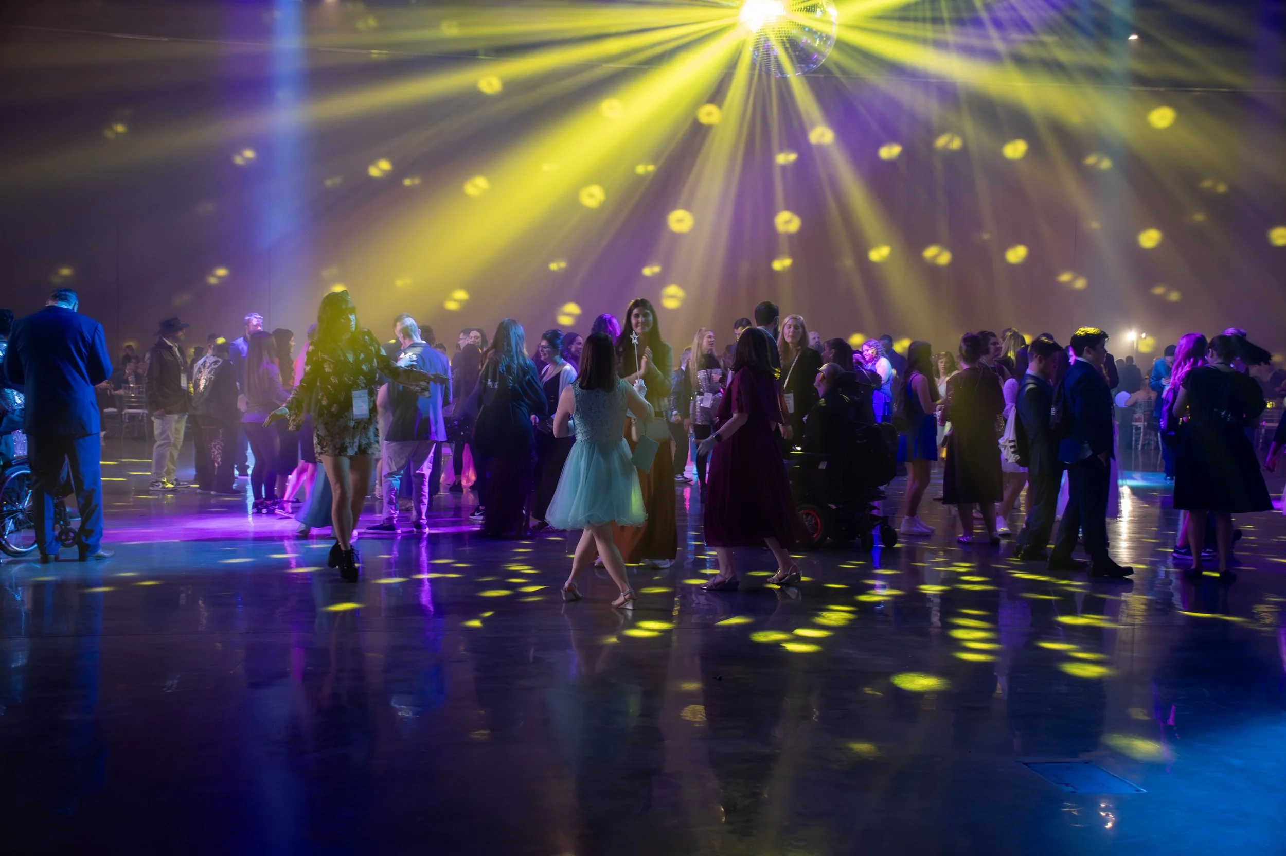 People dancing and socializing at a party with colorful lighting and a disco ball overhead.
