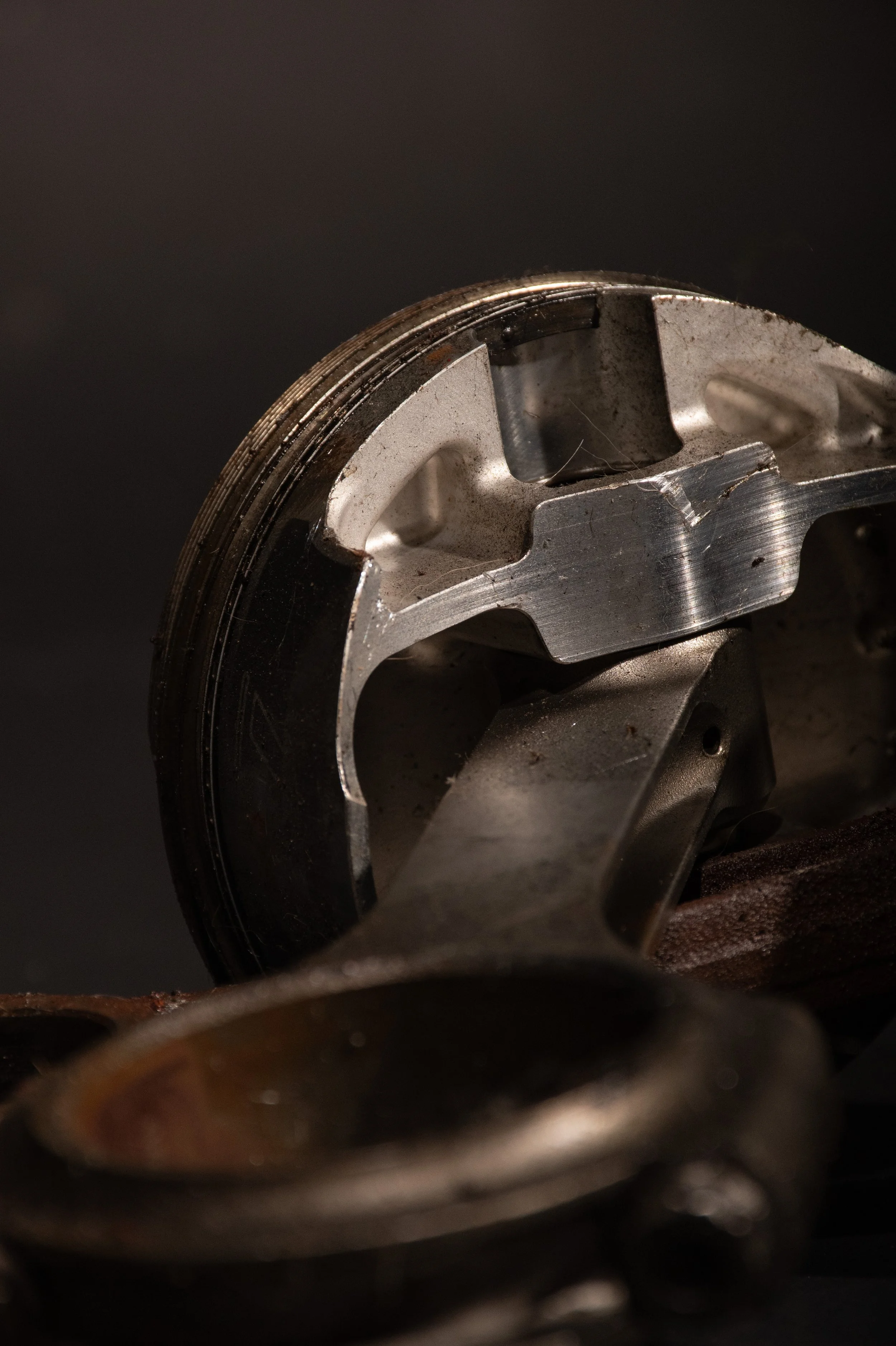 Close-up of a metal engine piston and connecting rod against a dark background.