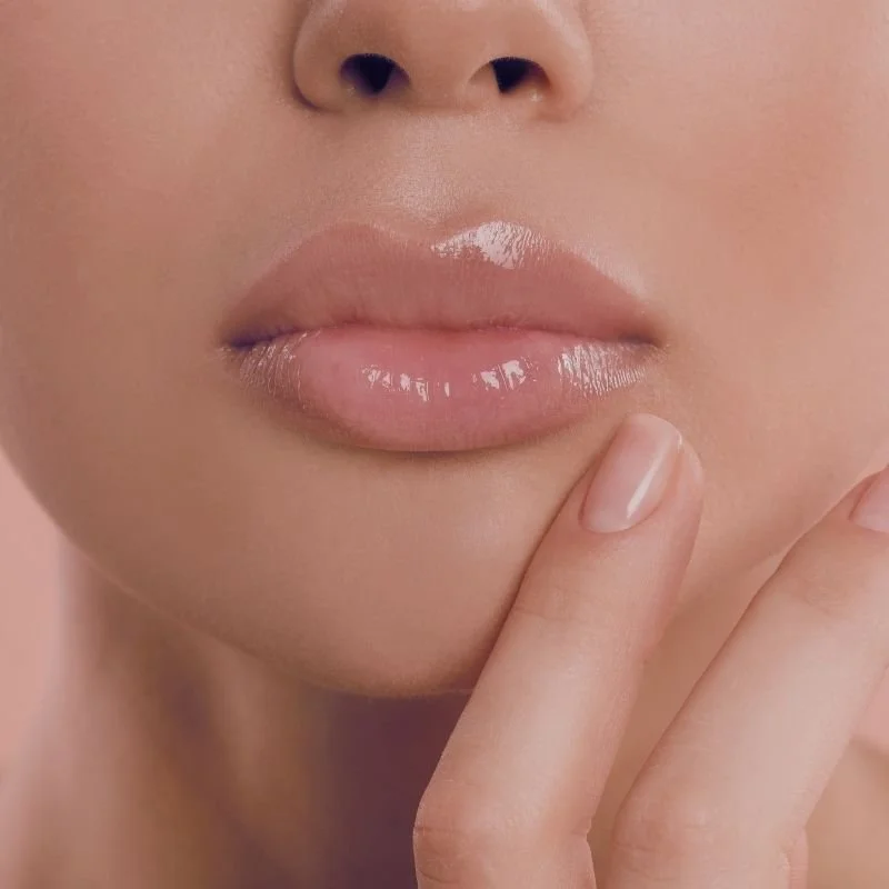 Close-up of a person's lips with glossy pink lipstick, and a finger touching the chin.