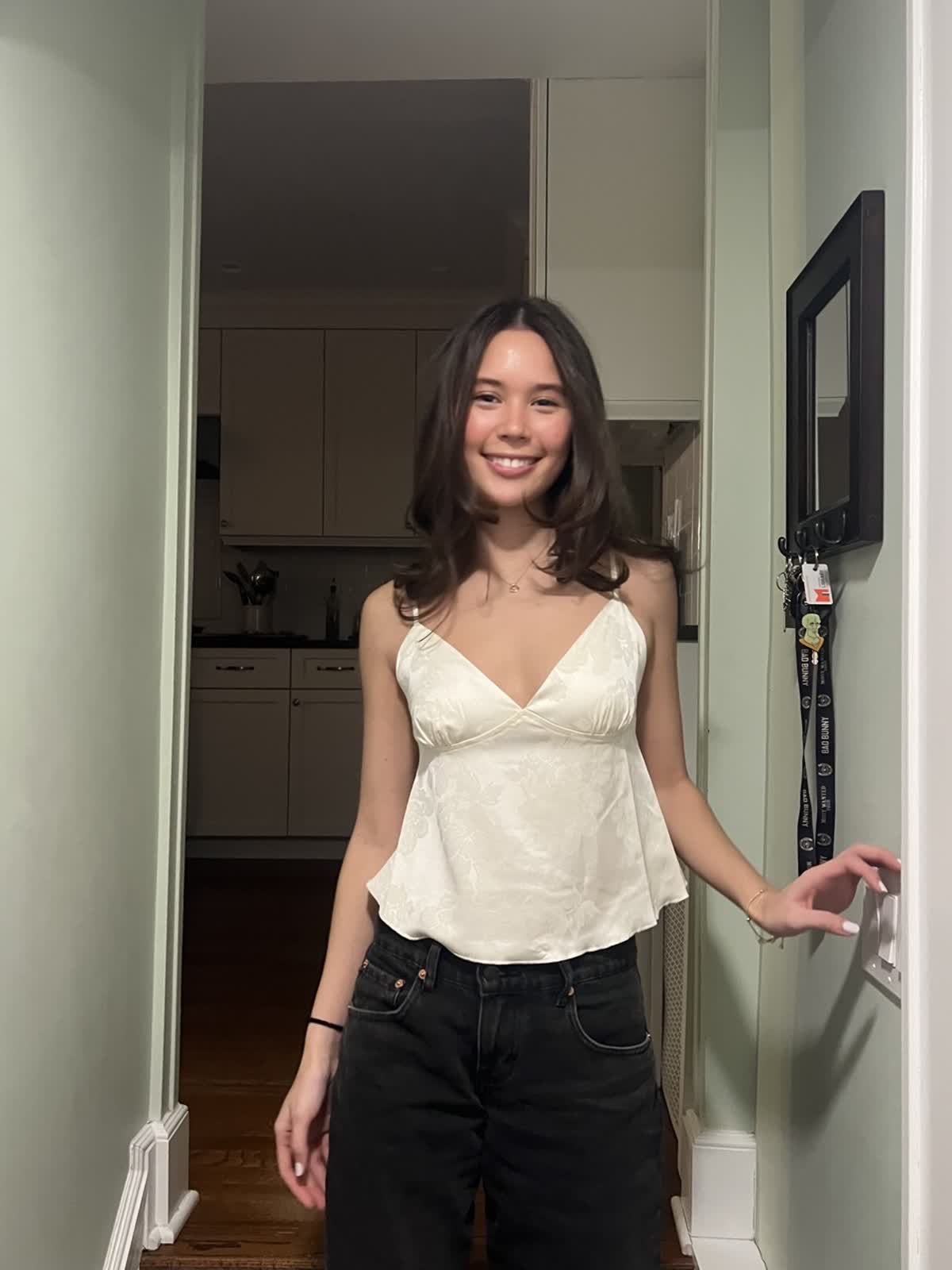 A young man sitting on hay in a farm field with green sunglasses, a black shirt, and a plaid jacket, with a tractor and other people in the background.