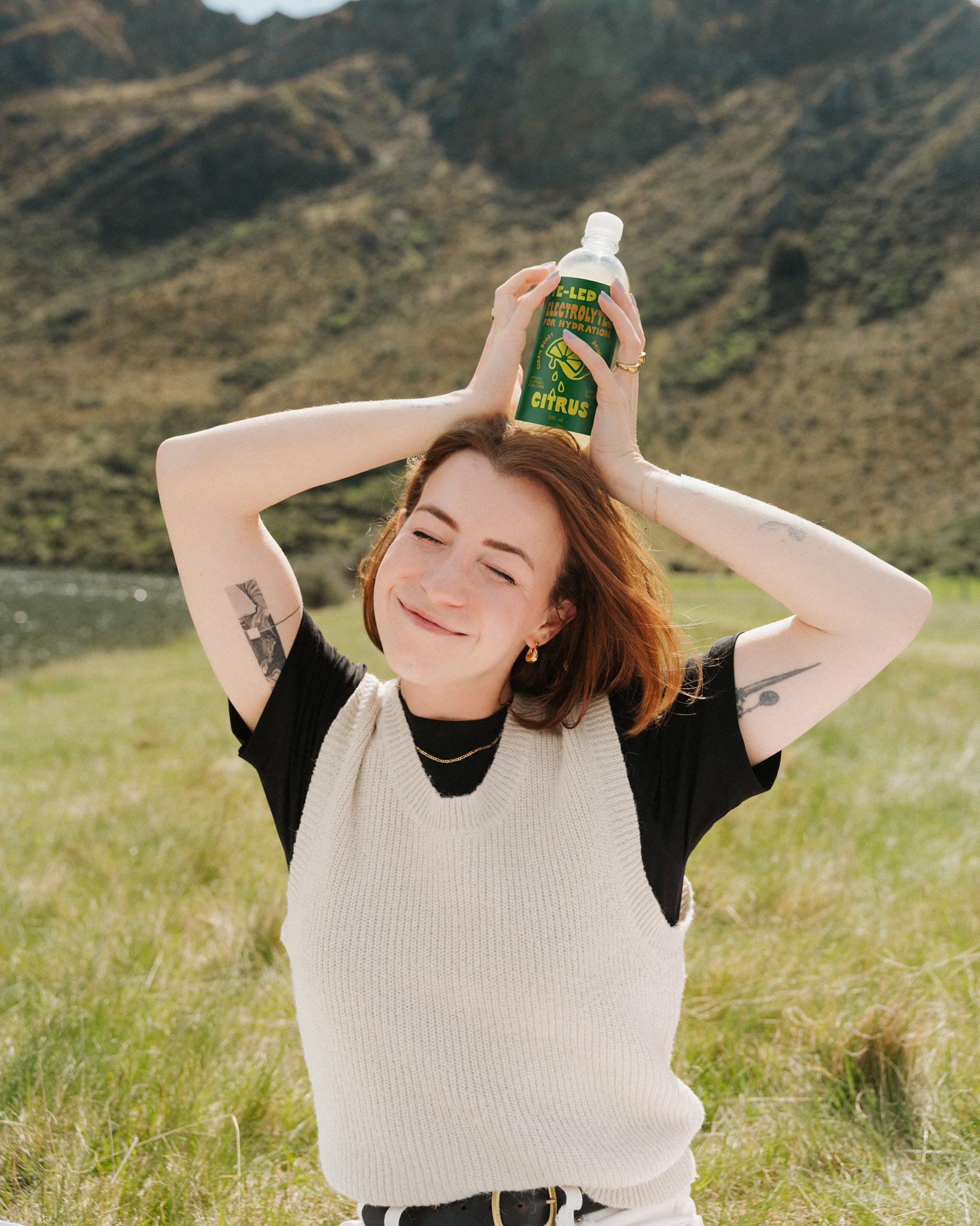 woman smiling and holding bottle of citrus te-ledoz on her head in a lake setting