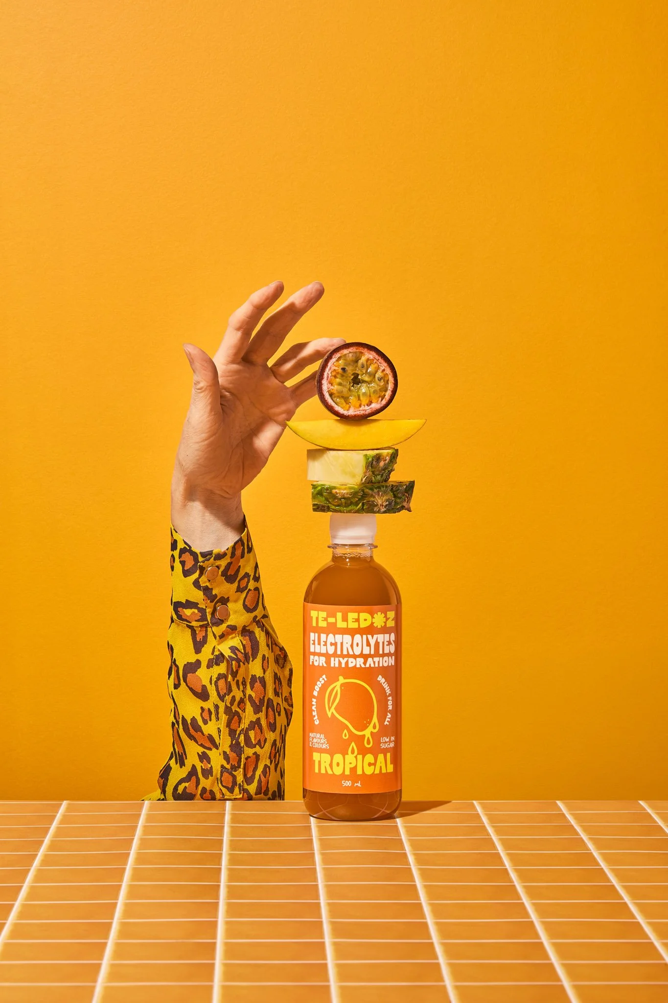 bottle of tropical flavour stacked with pineapple, mango and passionfruit, with a hand holding them up