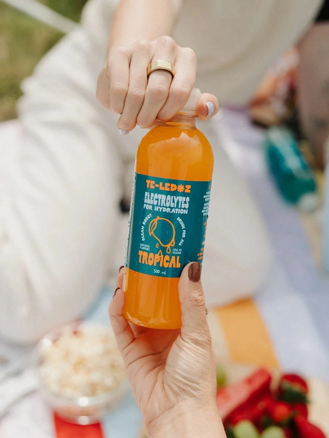 bottle of tropical te-ledoz with woman and picnic in the background